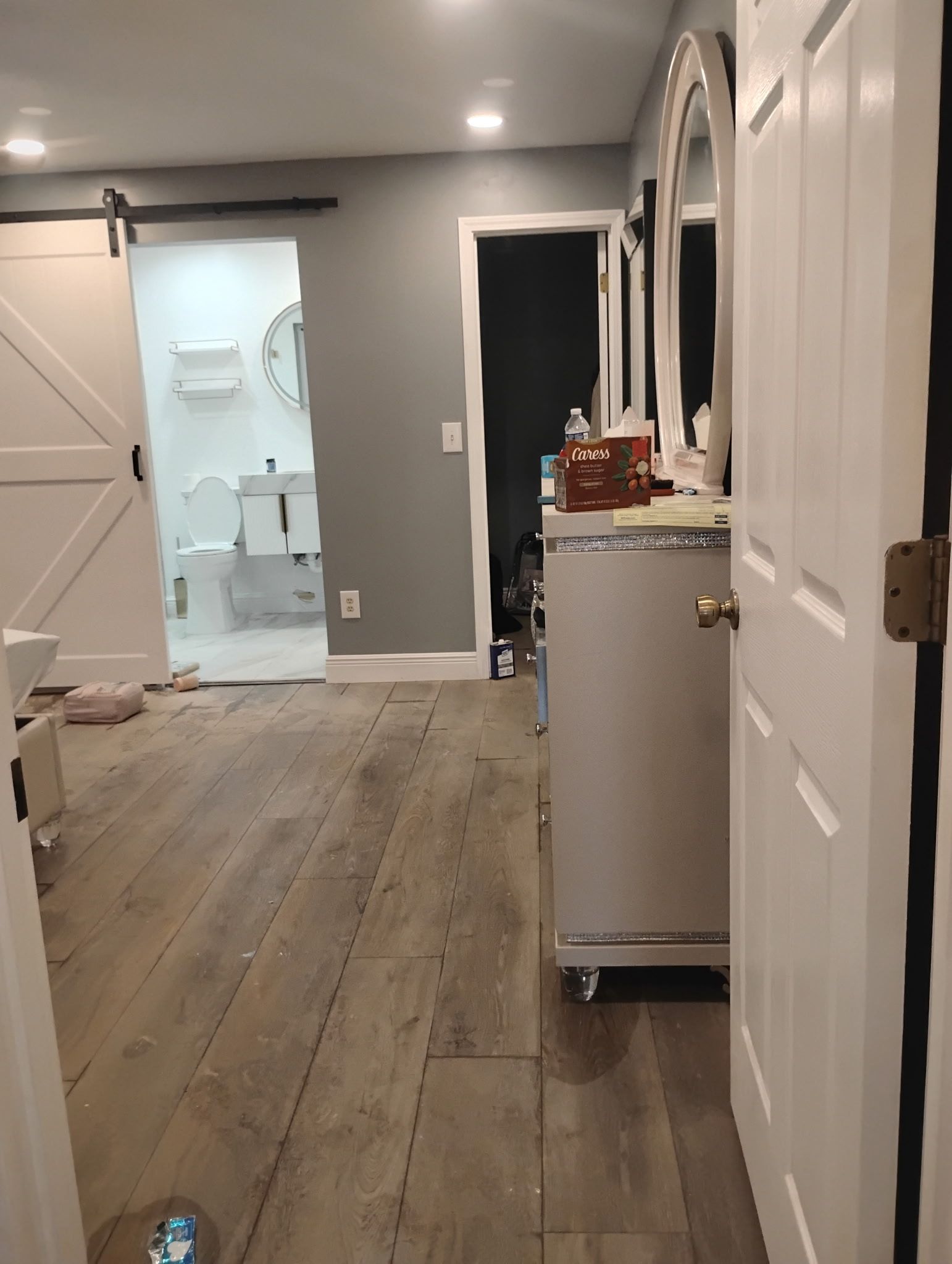 A bathroom with light wood flooring, a white cabinet, and a barn door leading to a toilet.