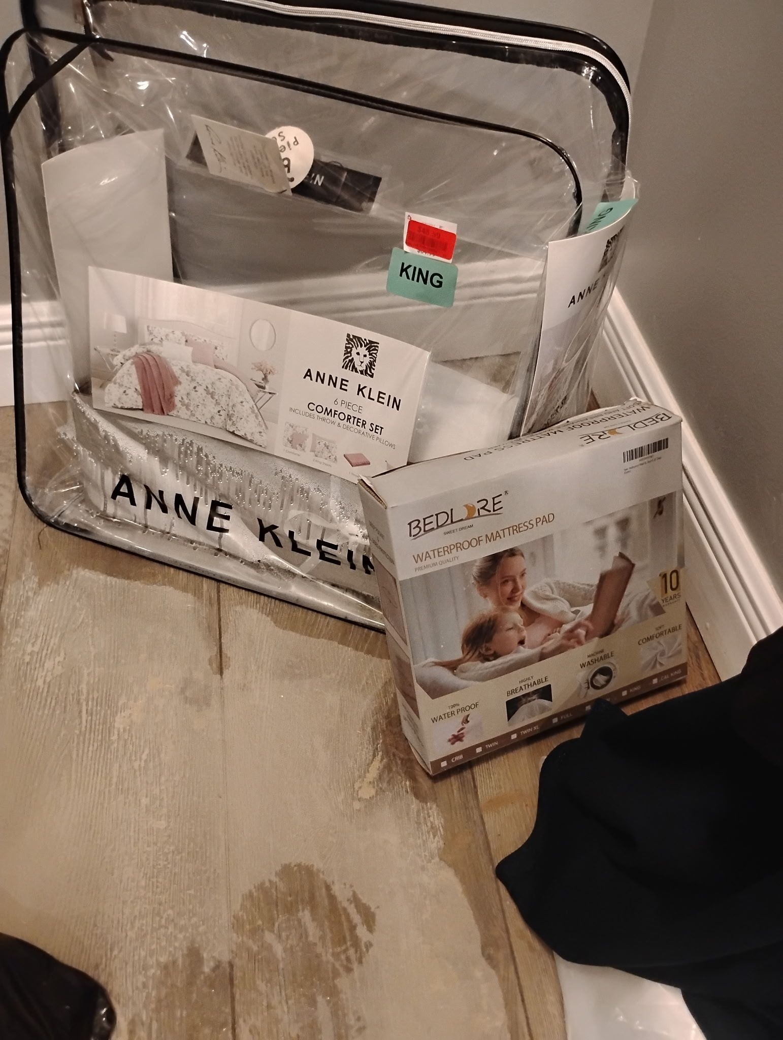 Clear Anne Klein tote with baby items on wooden floor.