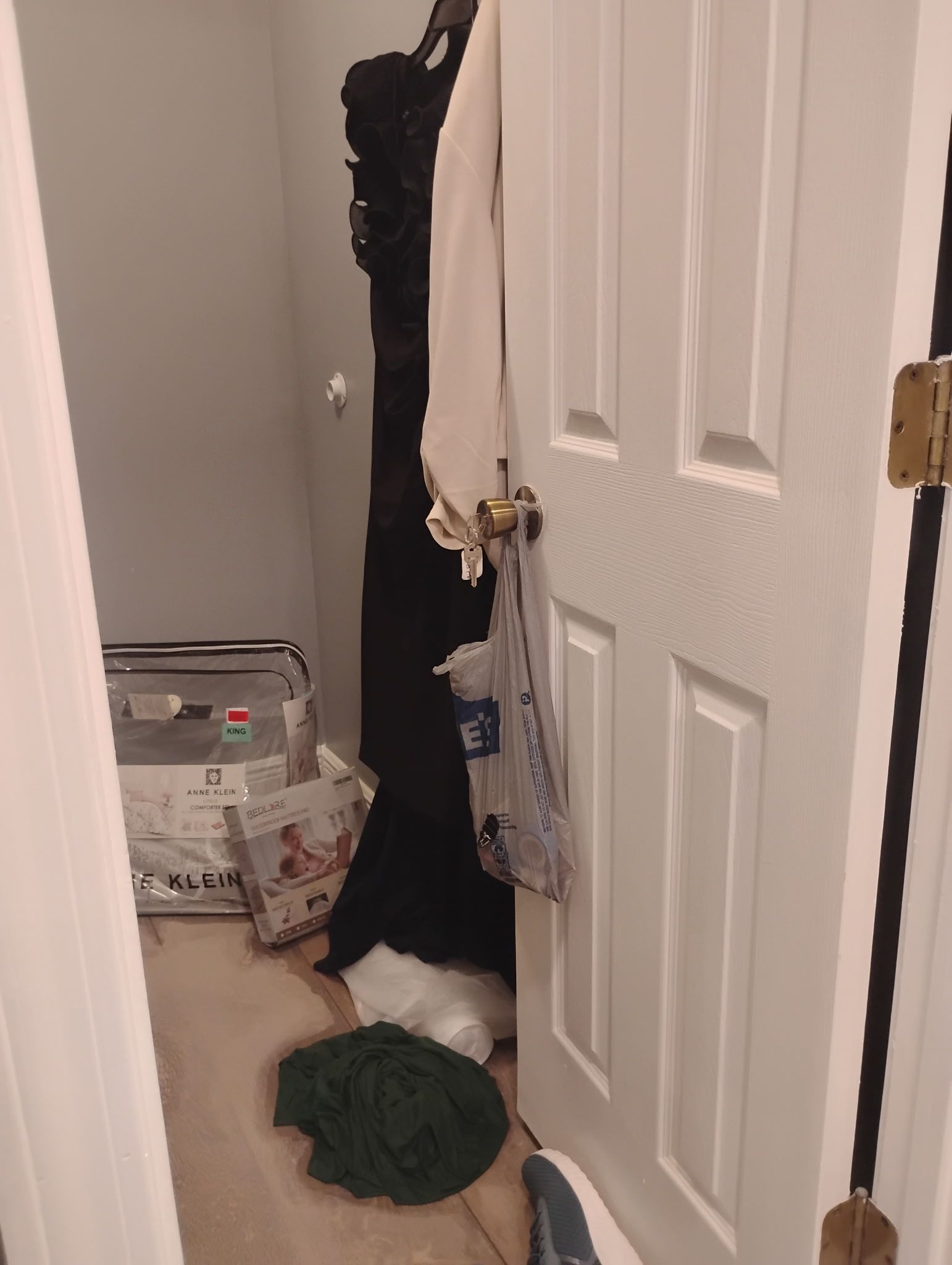 Ajar white door revealing a cluttered closet with clothes, bags, and items on the floor.