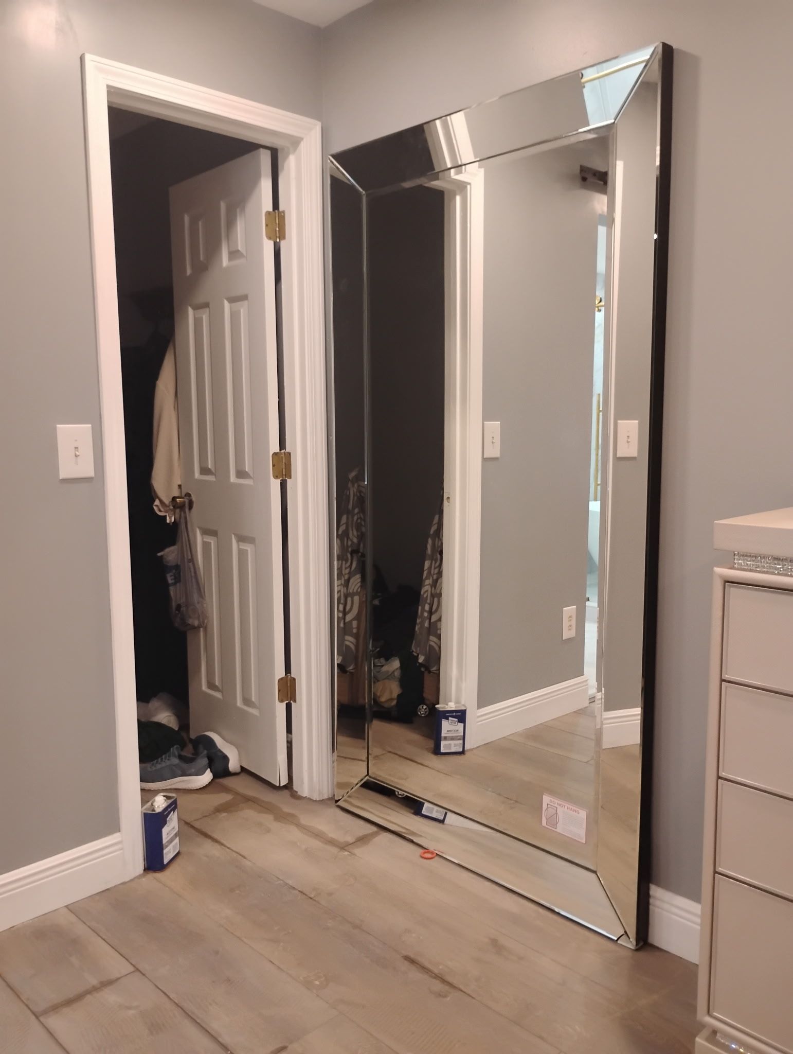 Large mirror reflecting a hallway and closet with an open door, placed against a gray wall.