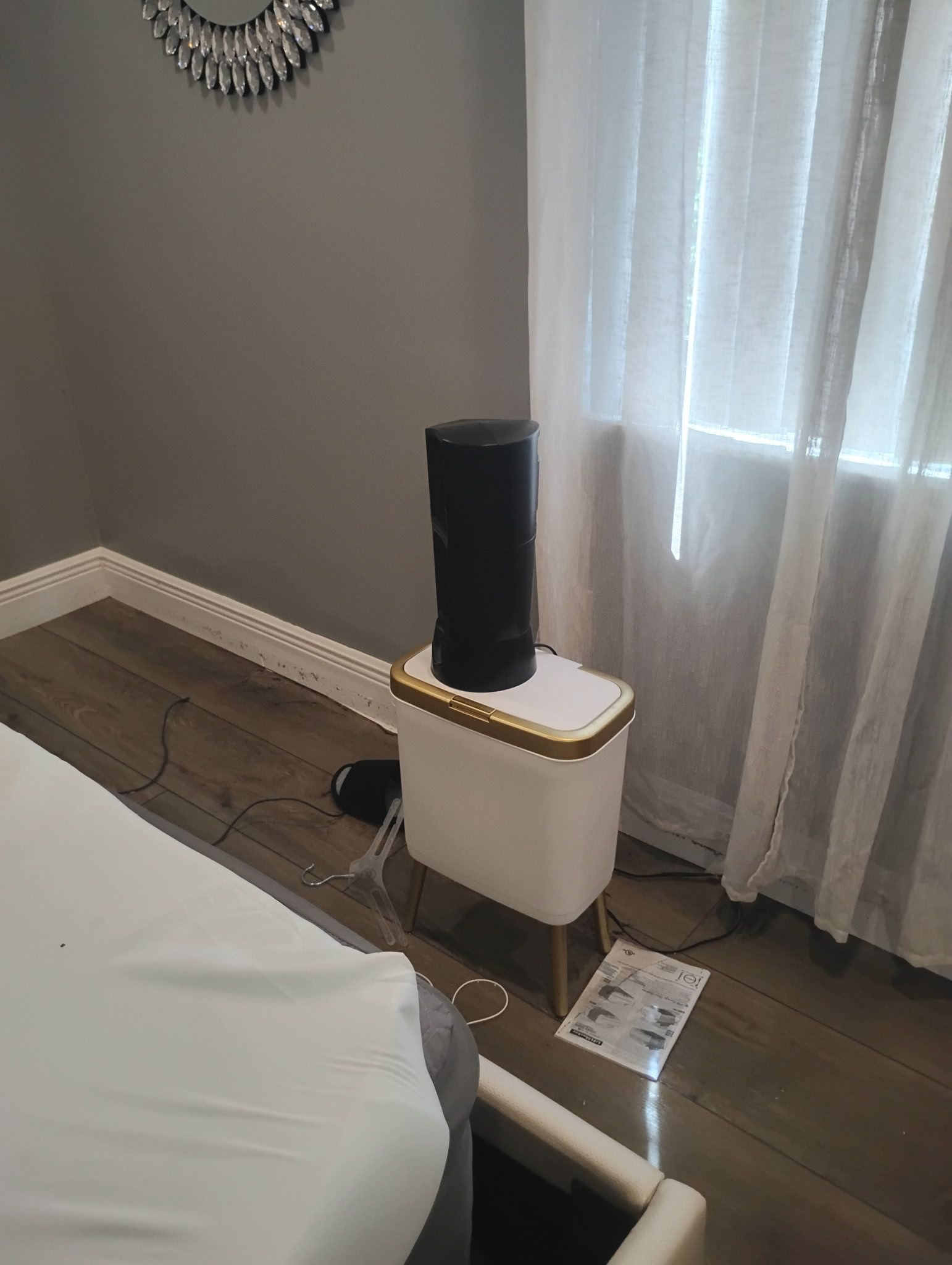 Black speaker on a white nightstand with gold trim, near a window with sheer curtains.