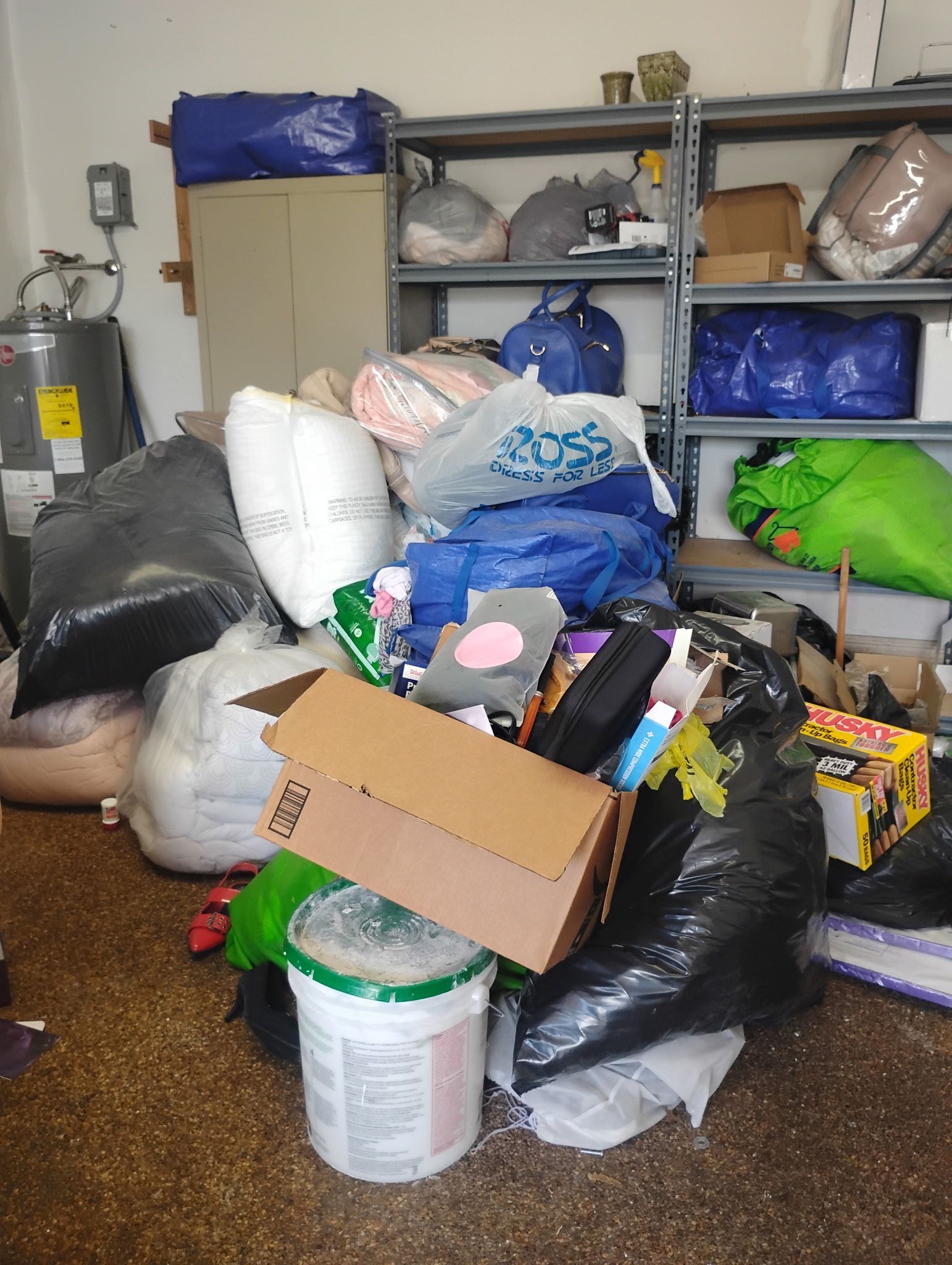Cluttered garage filled with trash bags, boxes, and miscellaneous items; shelves in the background.