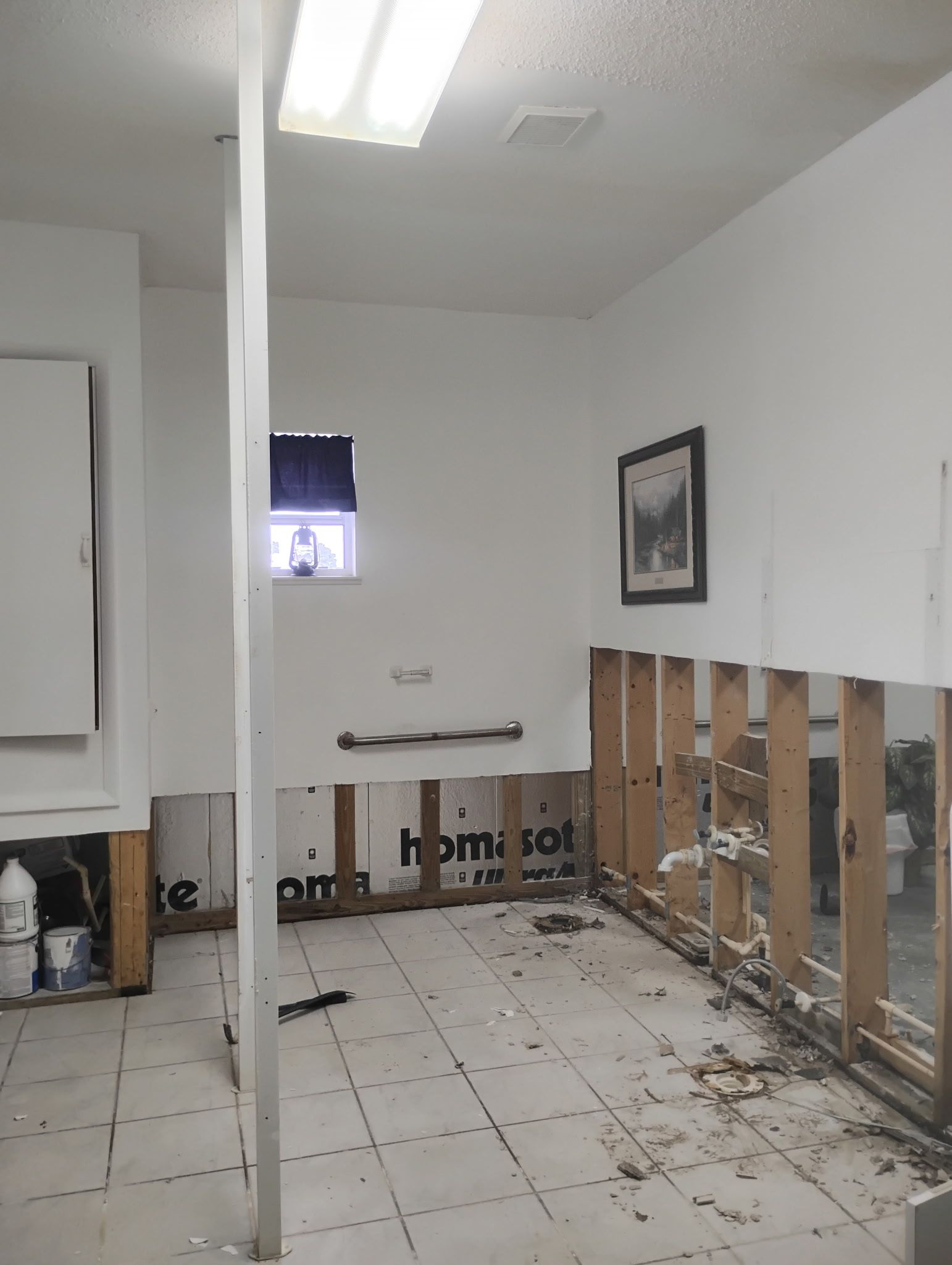 Bathroom interior undergoing renovation, exposed studs, partially removed wall and flooring, dirty floor.
