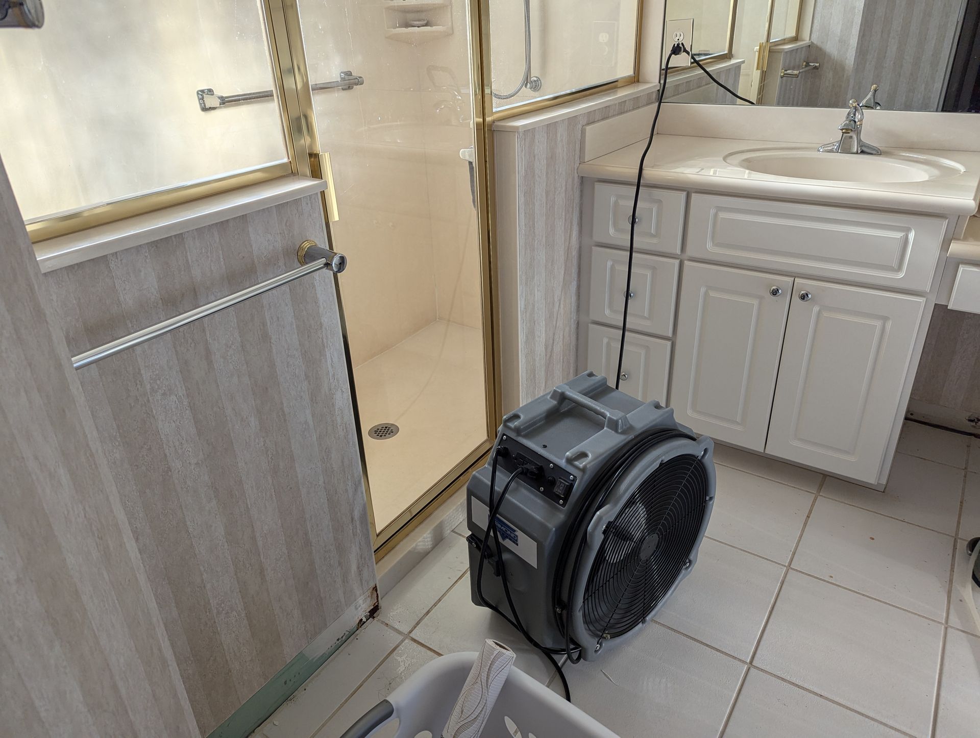 A bathroom with a laundry basket and a fan on the floor.
