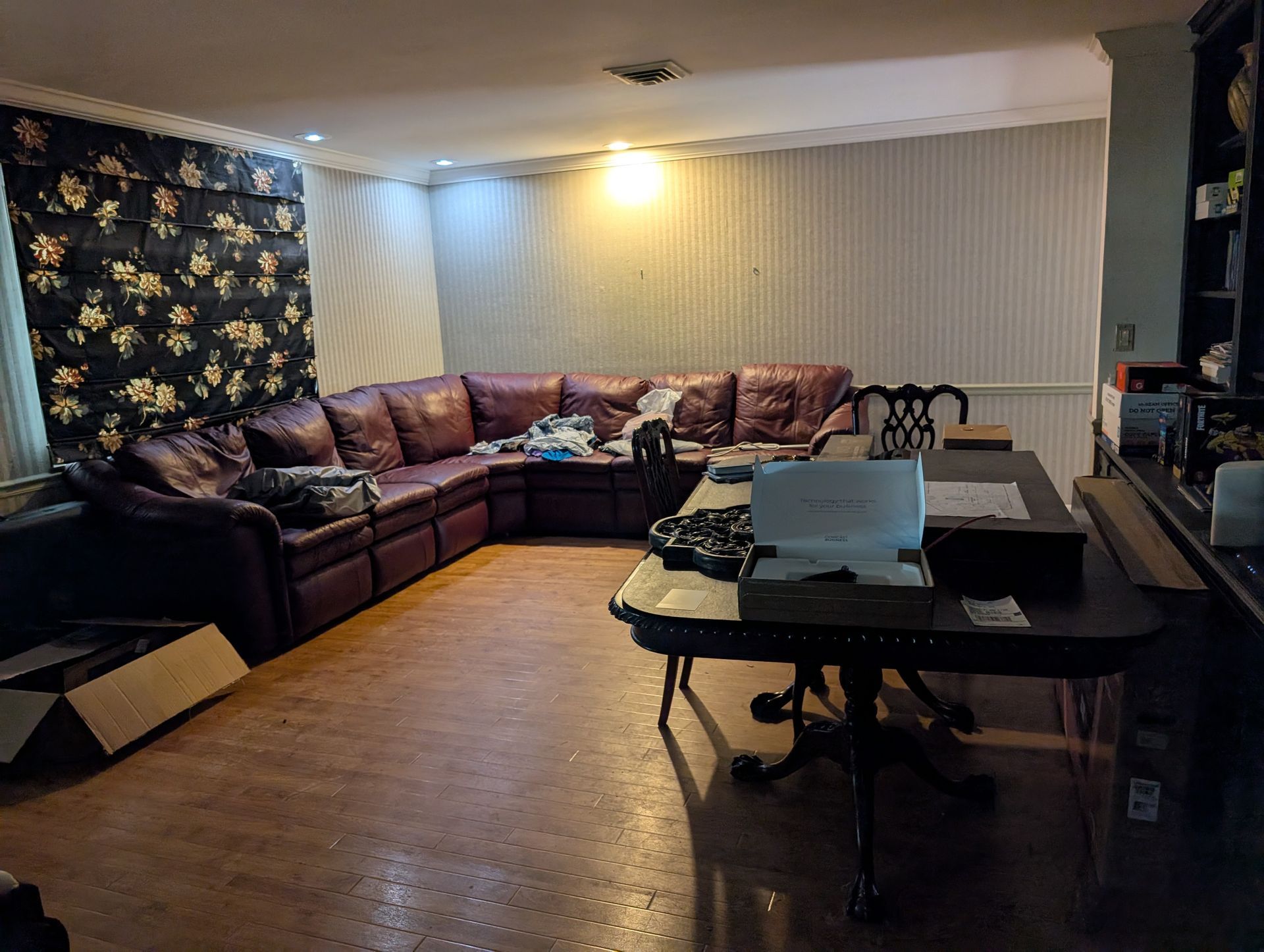 Living room with burgundy sectional sofa, desk, floral curtains, and wood flooring.