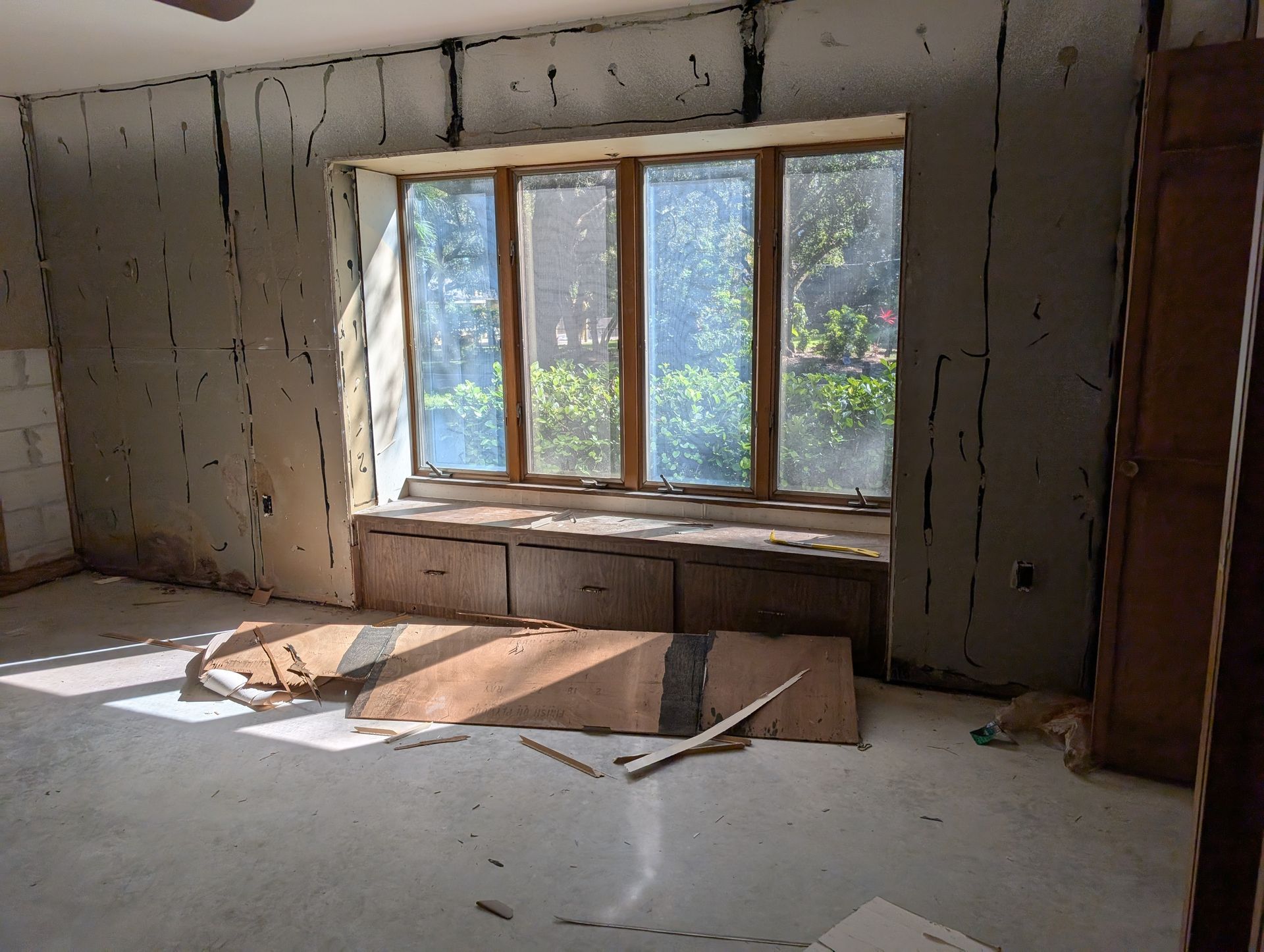 Interior room with window, cracked walls, and debris. Sunlight streams in.