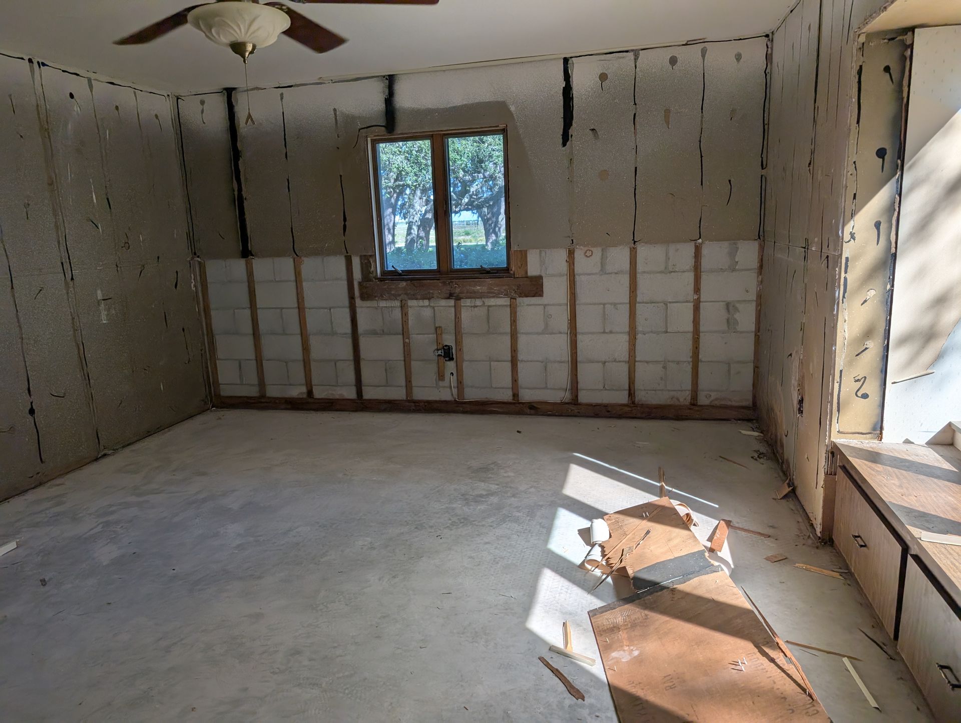 Room interior under renovation with exposed wall studs, concrete floor, and window.