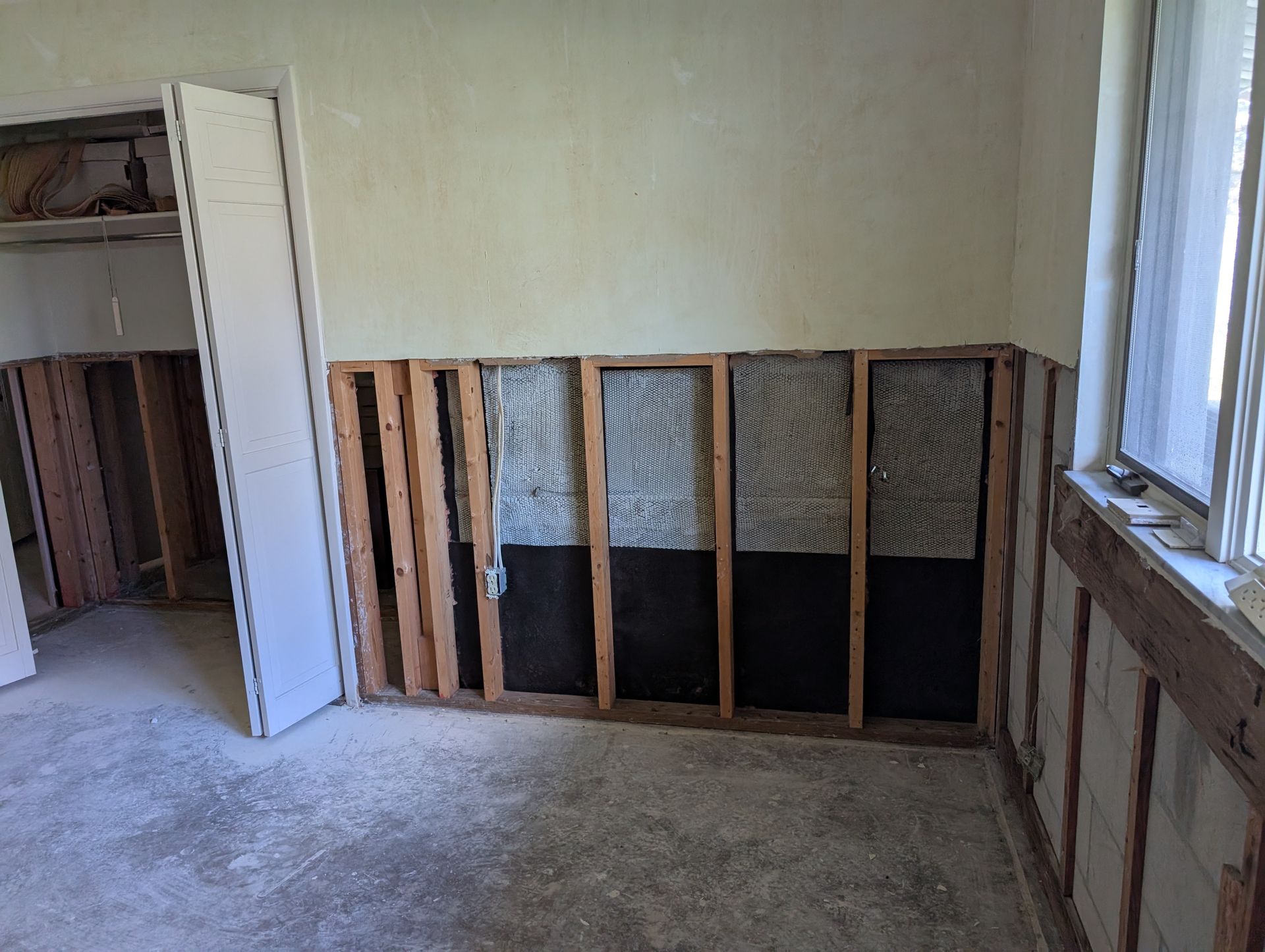Interior room undergoing renovation, exposed wall studs, insulation, and concrete floor.
