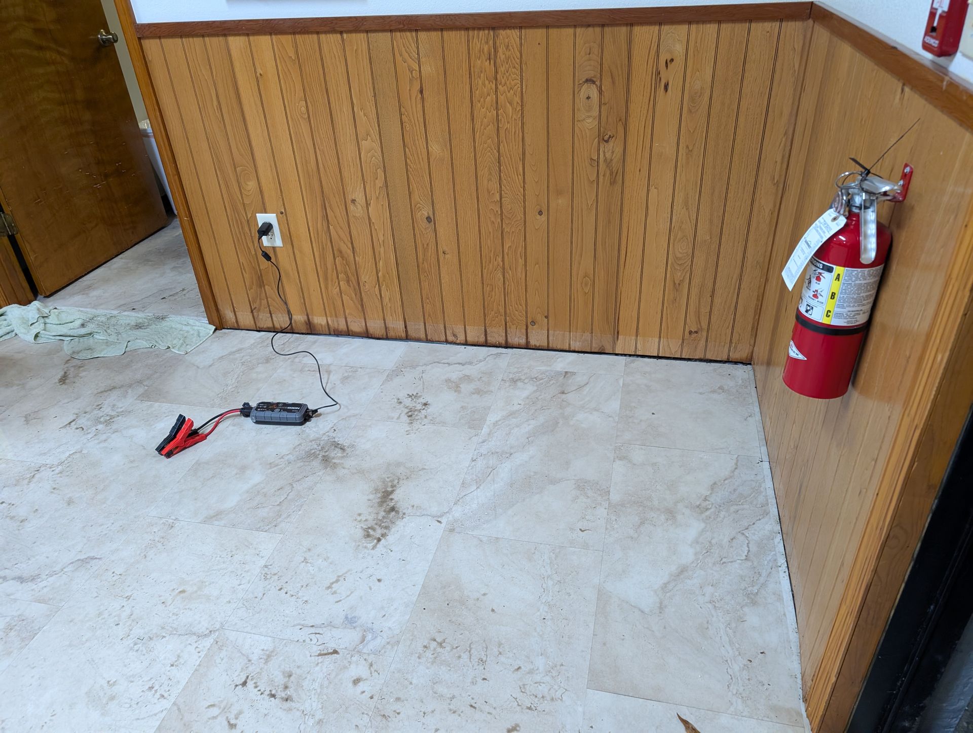 Corner of a room with wood paneling, tiled floor, fire extinguisher, and cables with clamps.