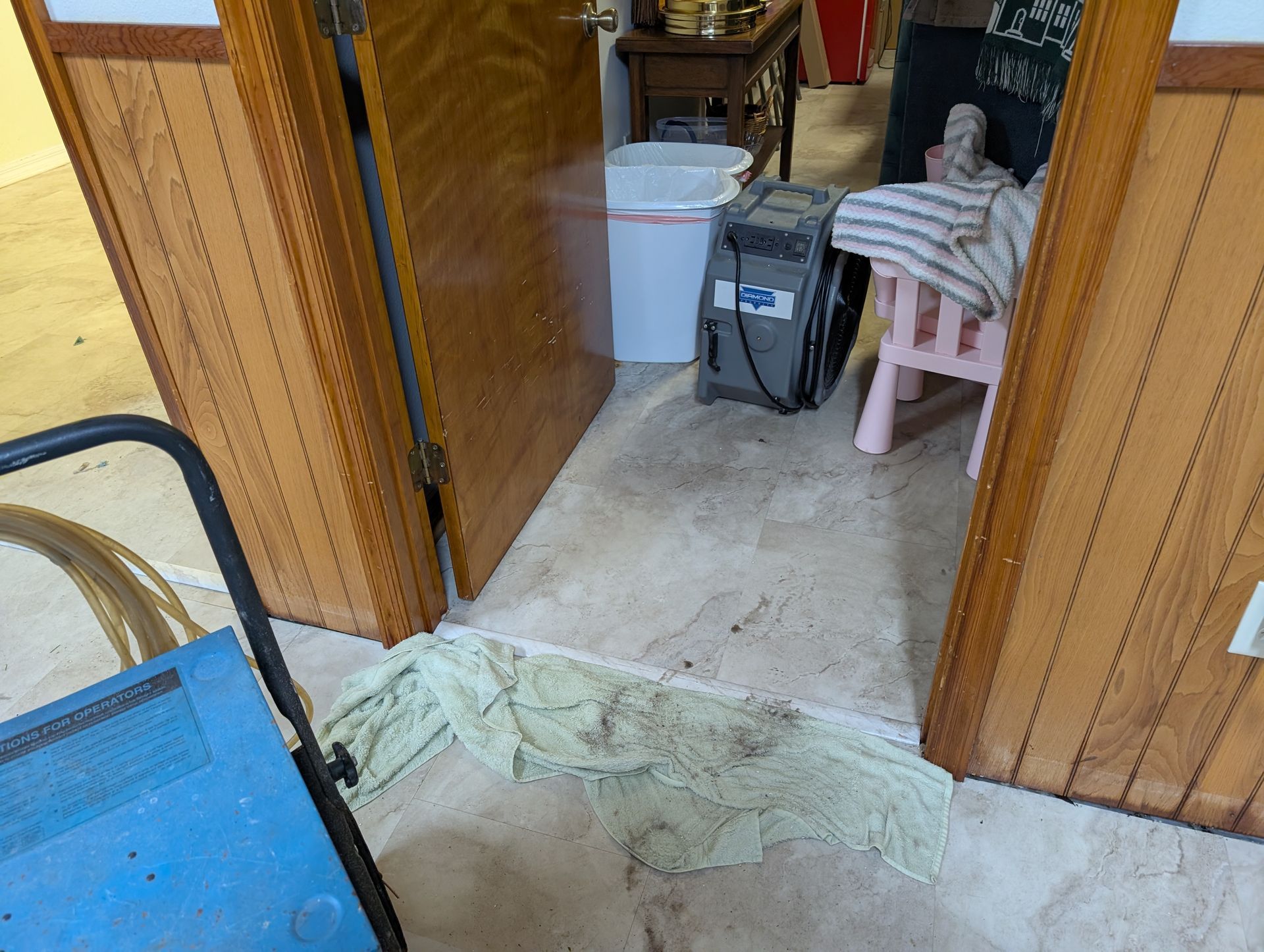 Open doorway with a drying machine, trash can, and small chair; debris on the floor.