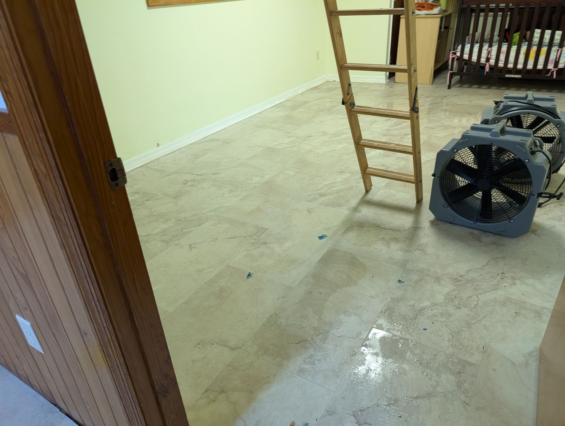 Room with a ladder, floor fans, and wet floor; door in the foreground.