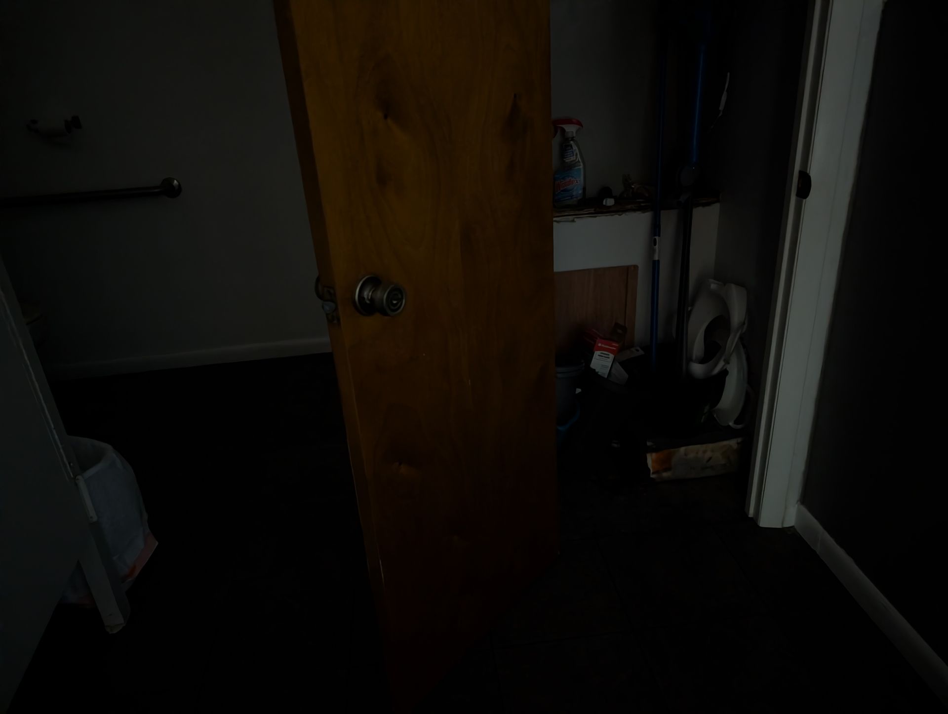 Wooden door slightly open into a dark room, dimly lit by an unseen light source.