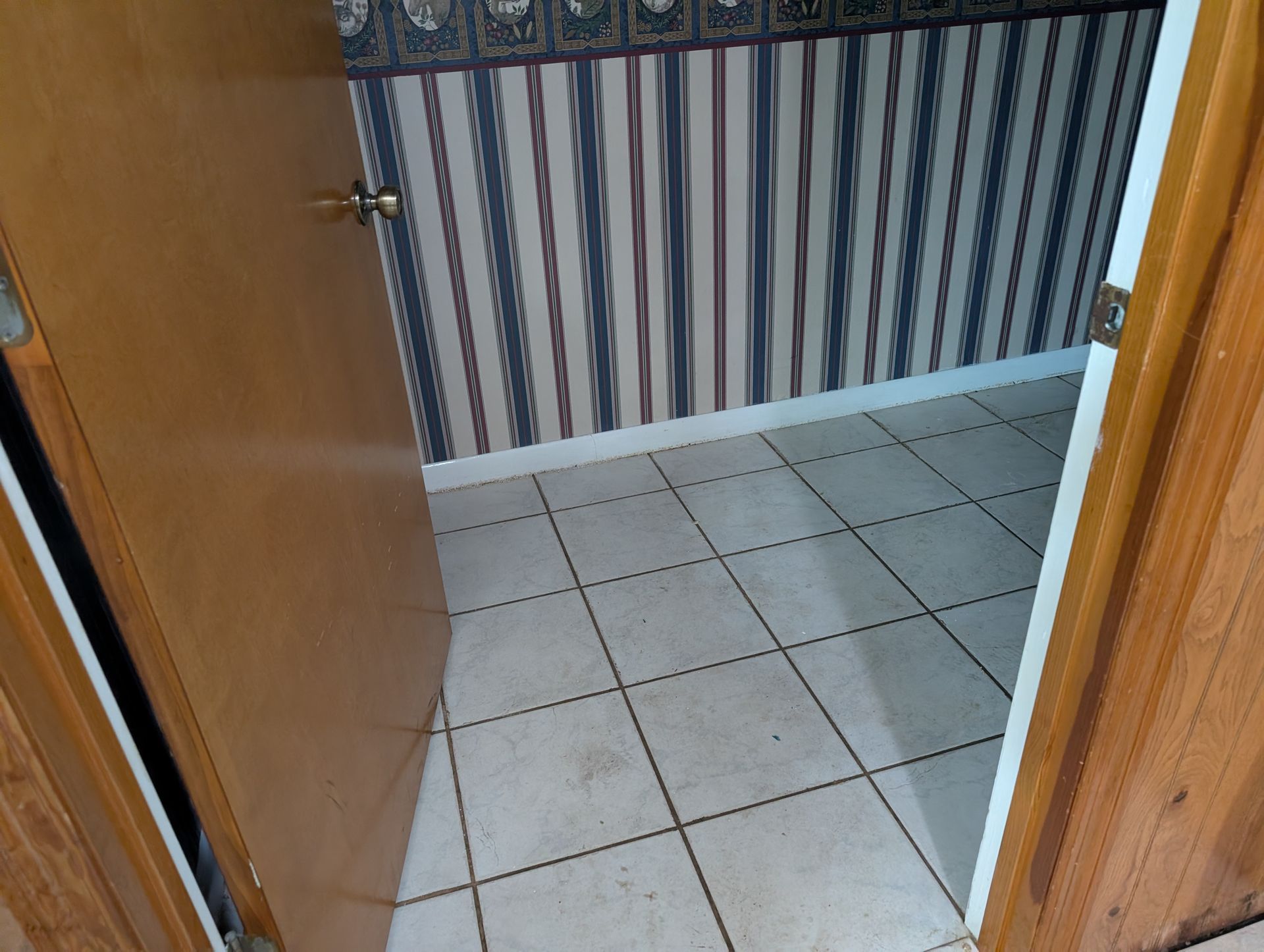 An open doorway to a small room with tiled floor and striped wallpaper.