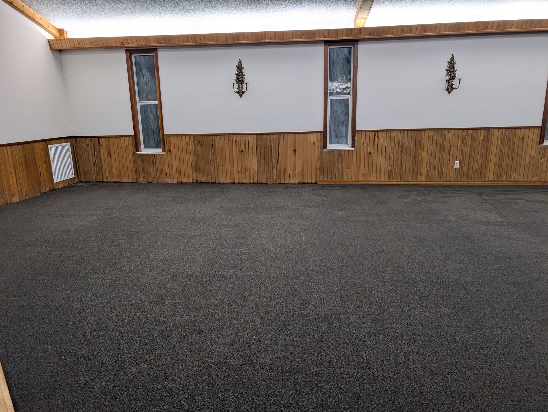 Empty room with gray textured floor, wood paneling, white walls, and small windows.