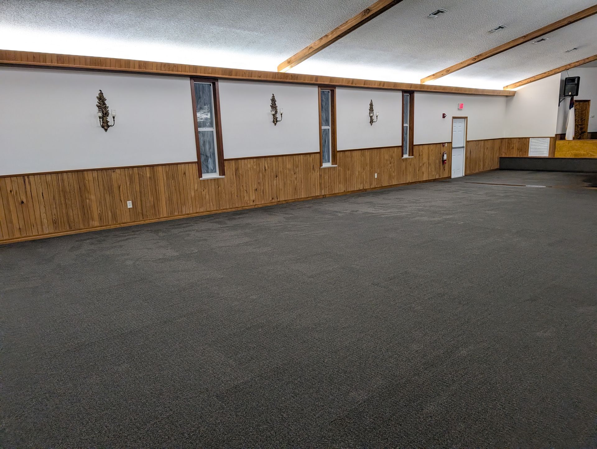 Empty event space with dark gray floor, wood paneling, and white walls.