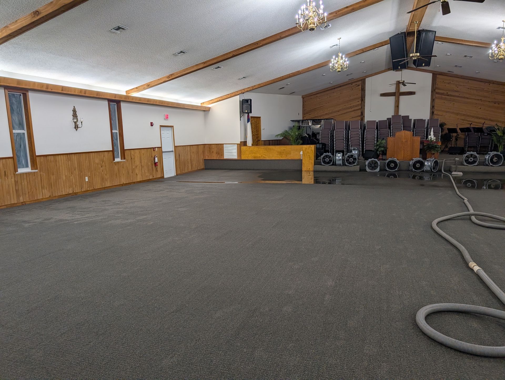 Interior view of a church, showing an empty carpeted floor, stage, pews, and cross.