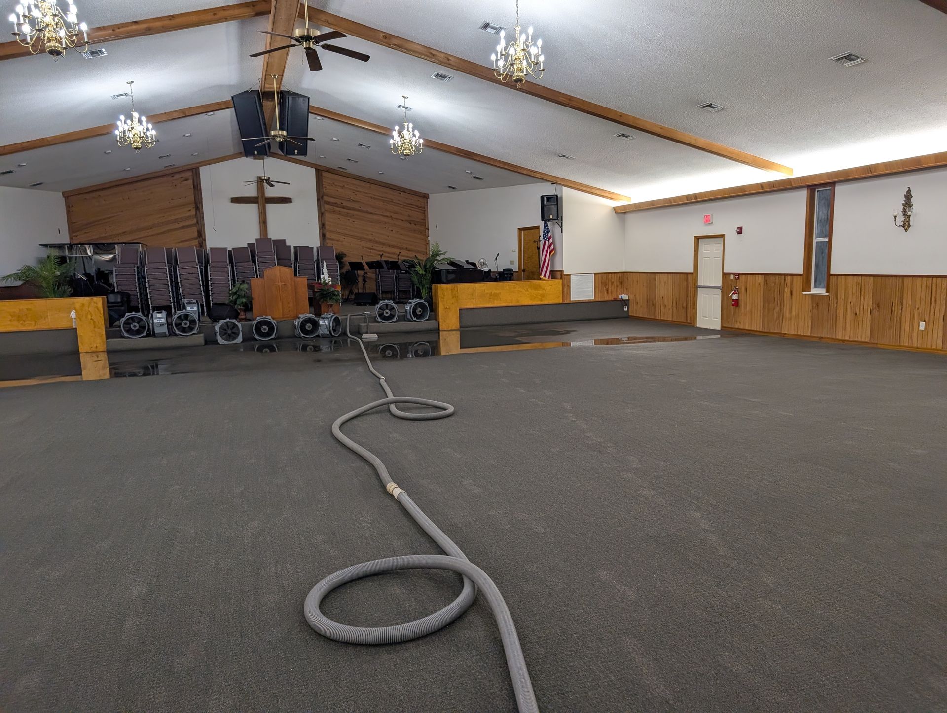 Interior of a church sanctuary, with a long hose snaking across the carpeted floor.