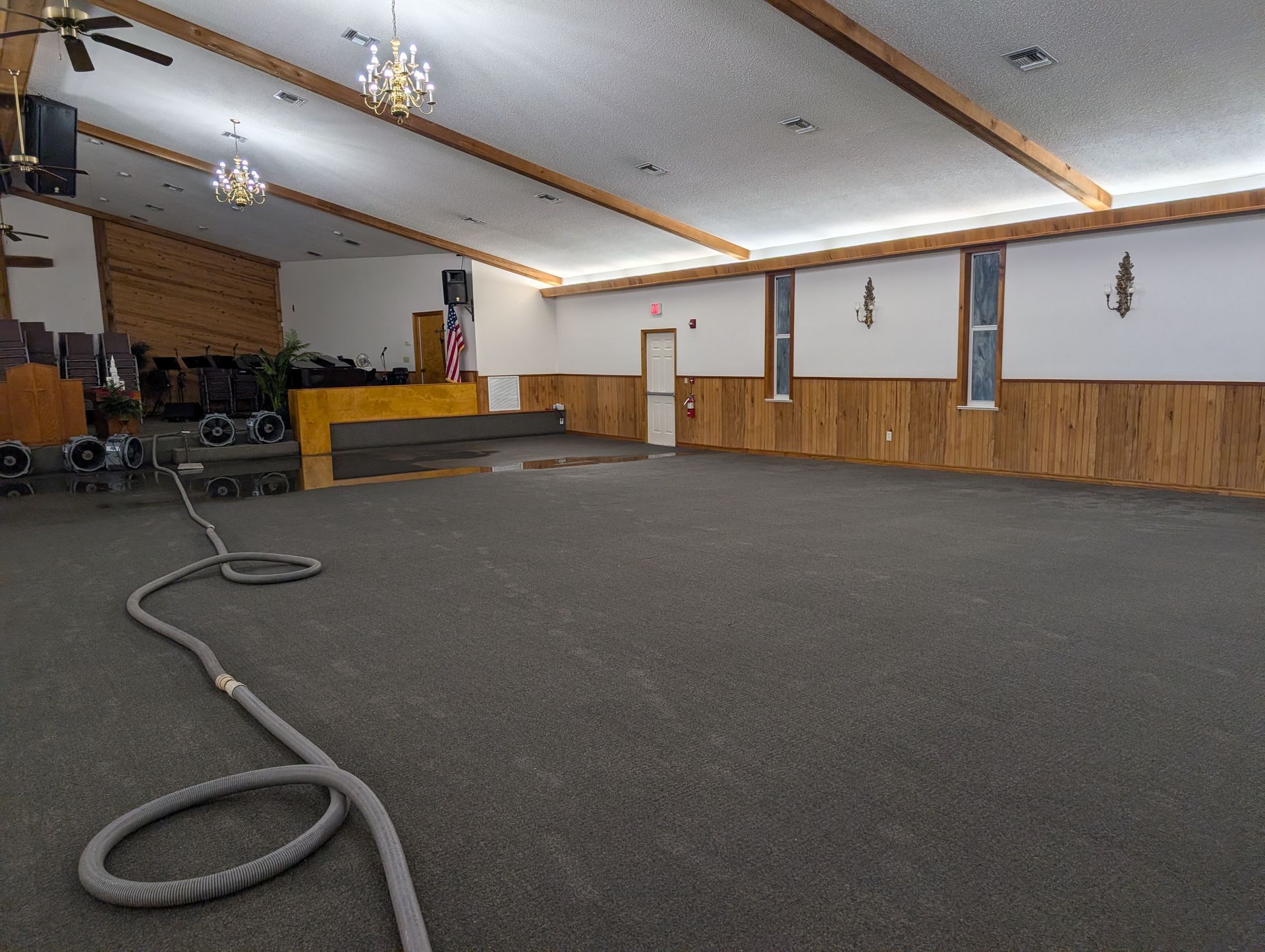 Empty room with gray carpet, wood accents, and ceiling lights, possibly a church or event space.