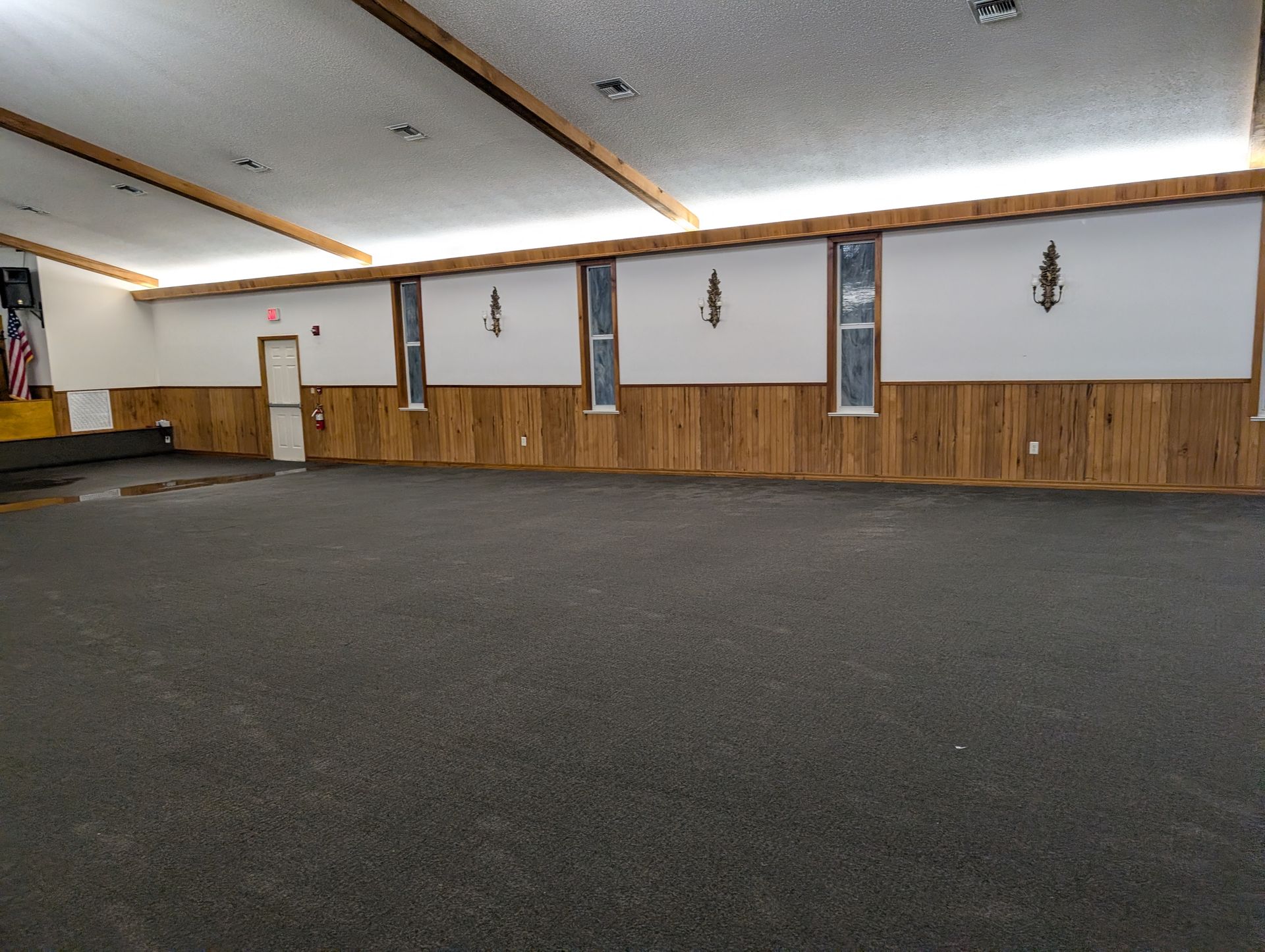 Empty room with dark carpet, wood paneling, and white walls. Small windows are spaced along one wall.