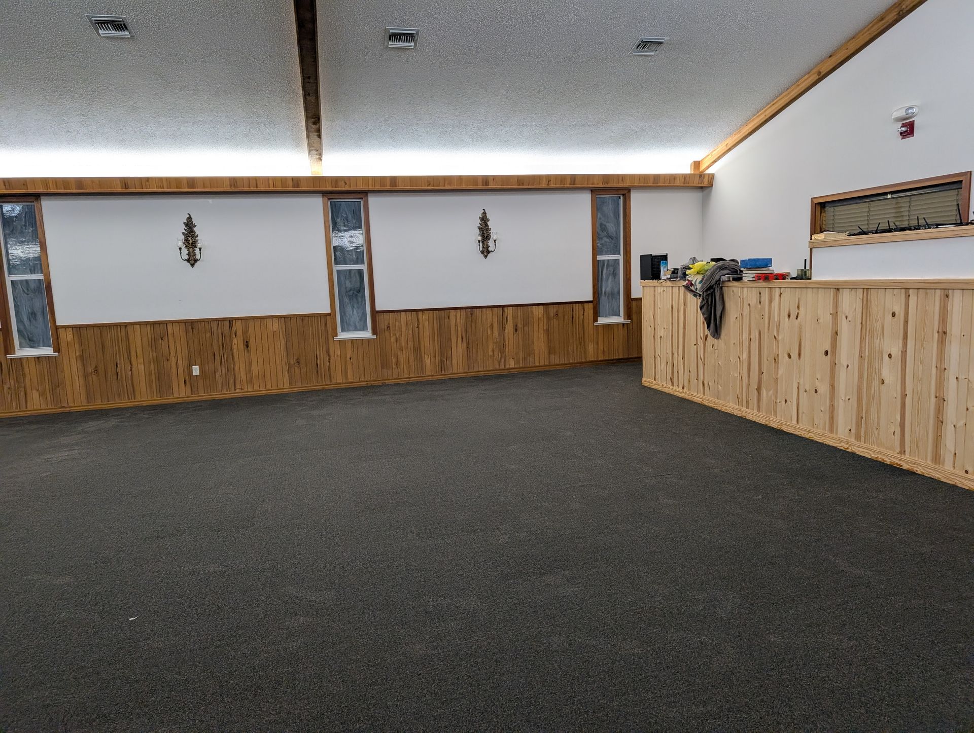 Empty event space with brown paneling, dark carpet, and white walls.