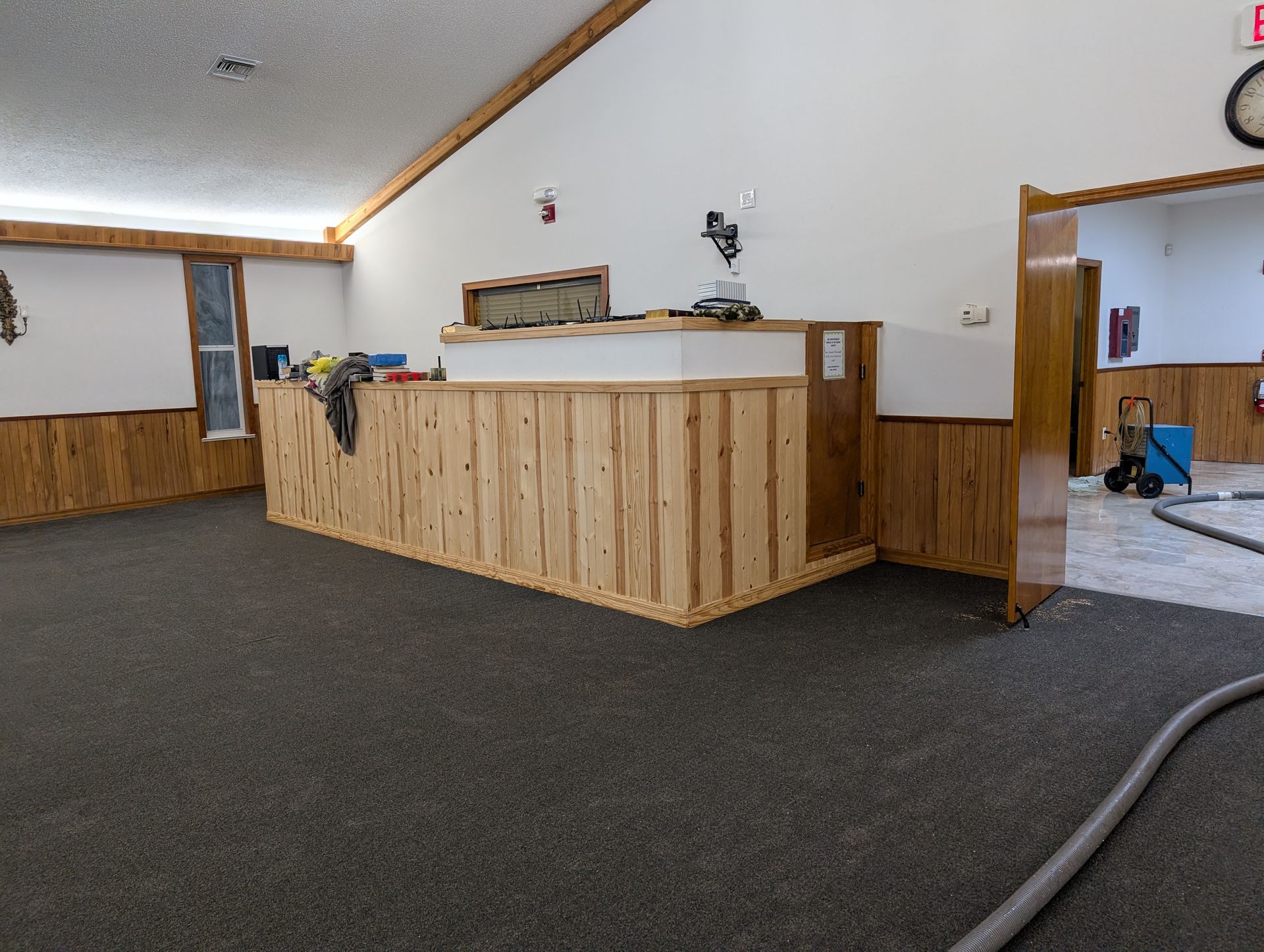 Interior view: reception desk with wood paneling, tools, and dark carpet flooring.