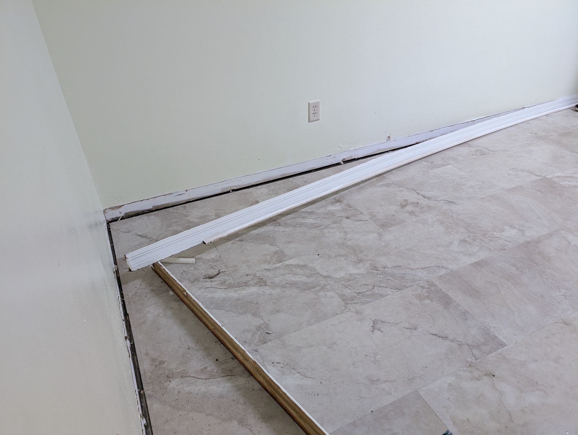 Room under construction; white trim pieces on floor and against light green wall. Beige tile flooring.