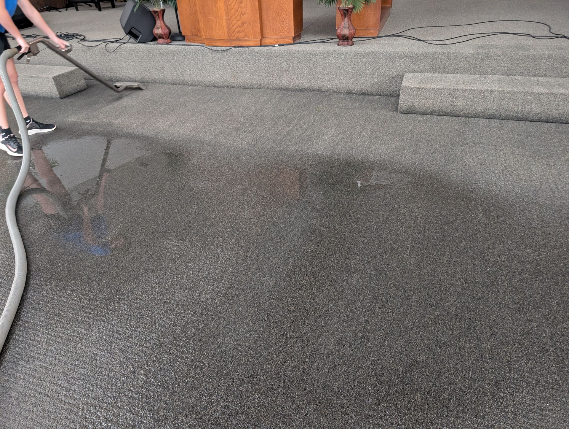 Person using a hose to wash a dark gray aggregate surface in an outdoor setting.