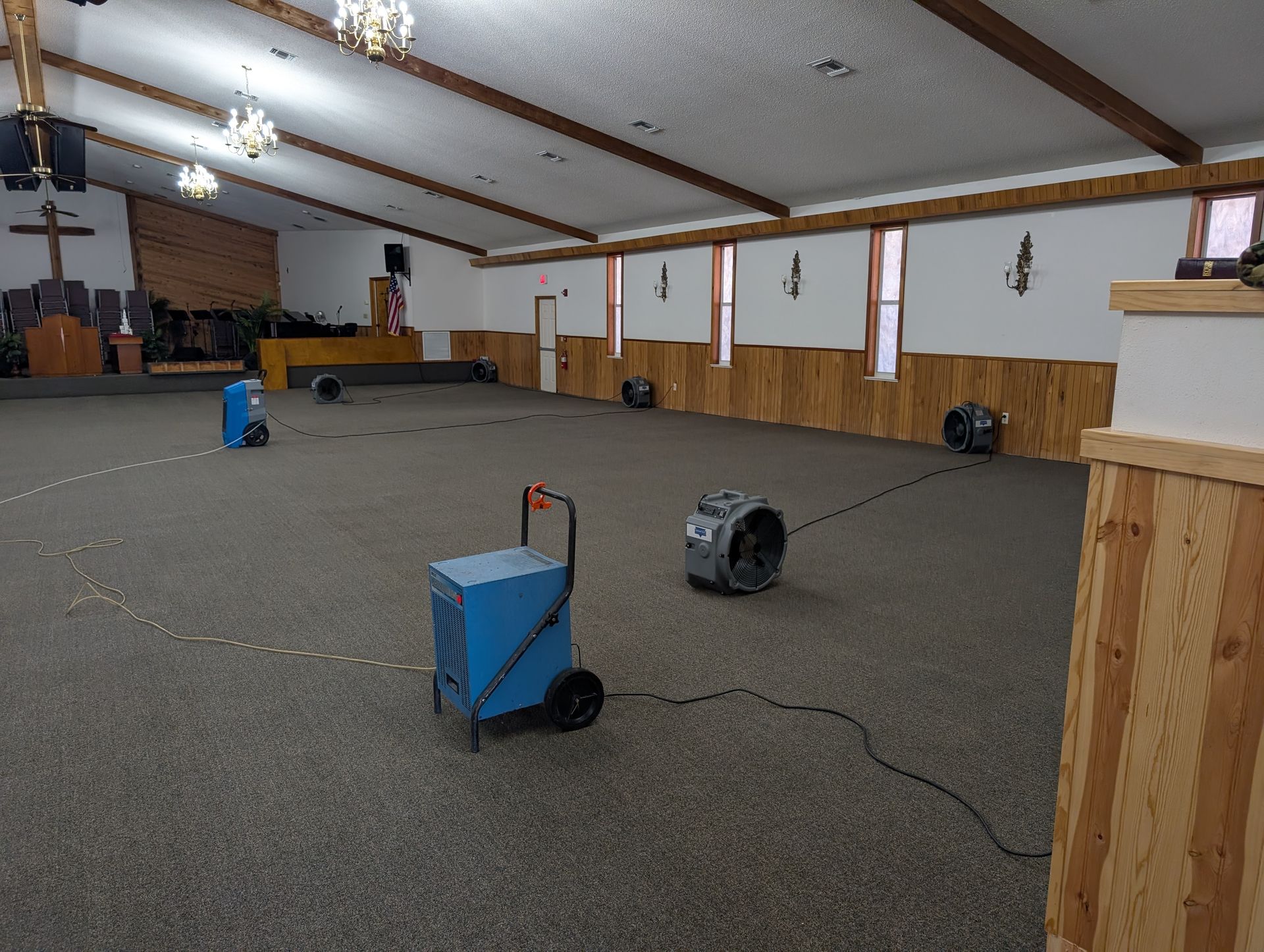 Church interior with several dehumidifiers and fans on the carpeted floor.