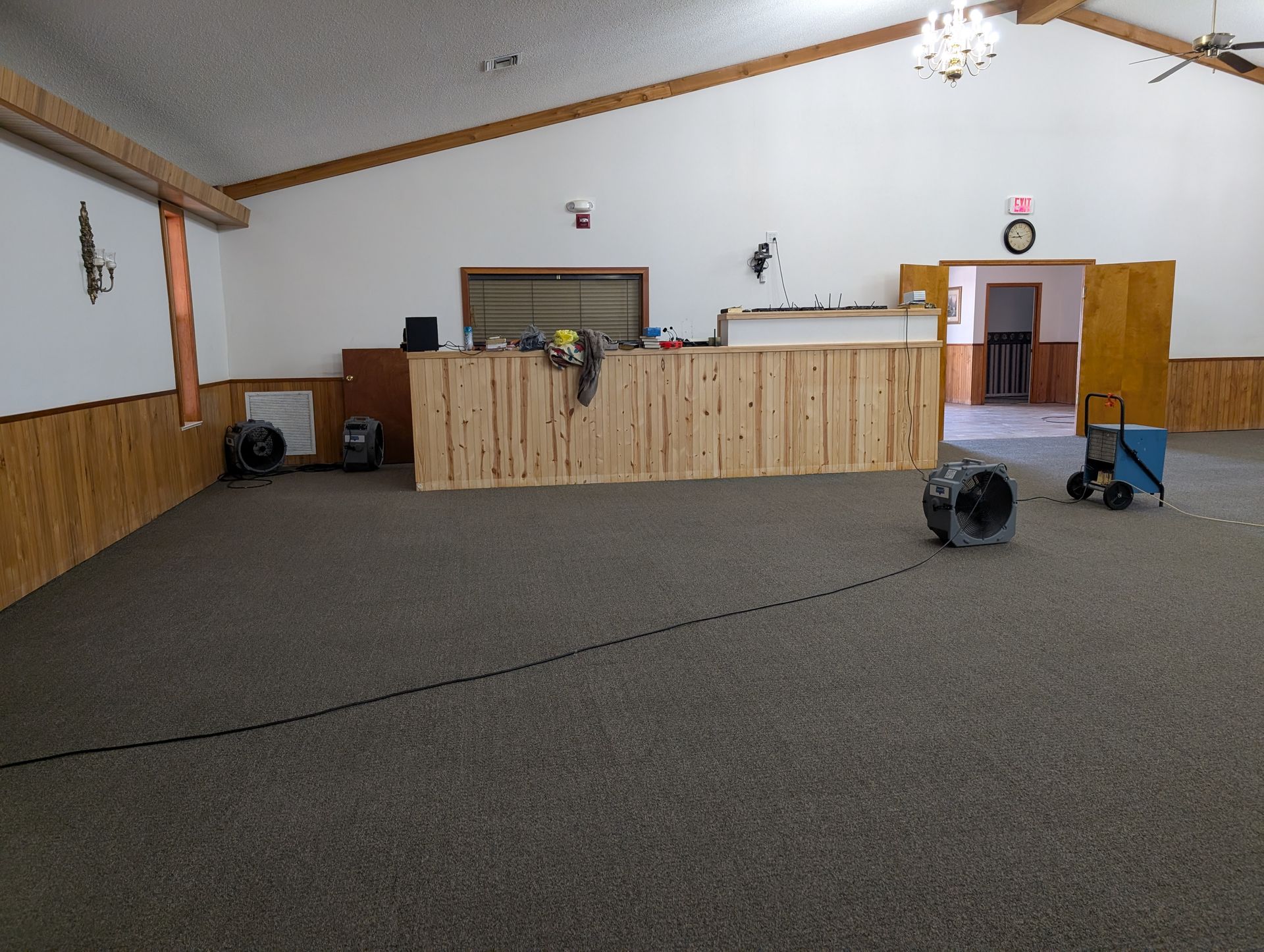 Empty event hall with carpet, wooden bar, and equipment set up for drying.