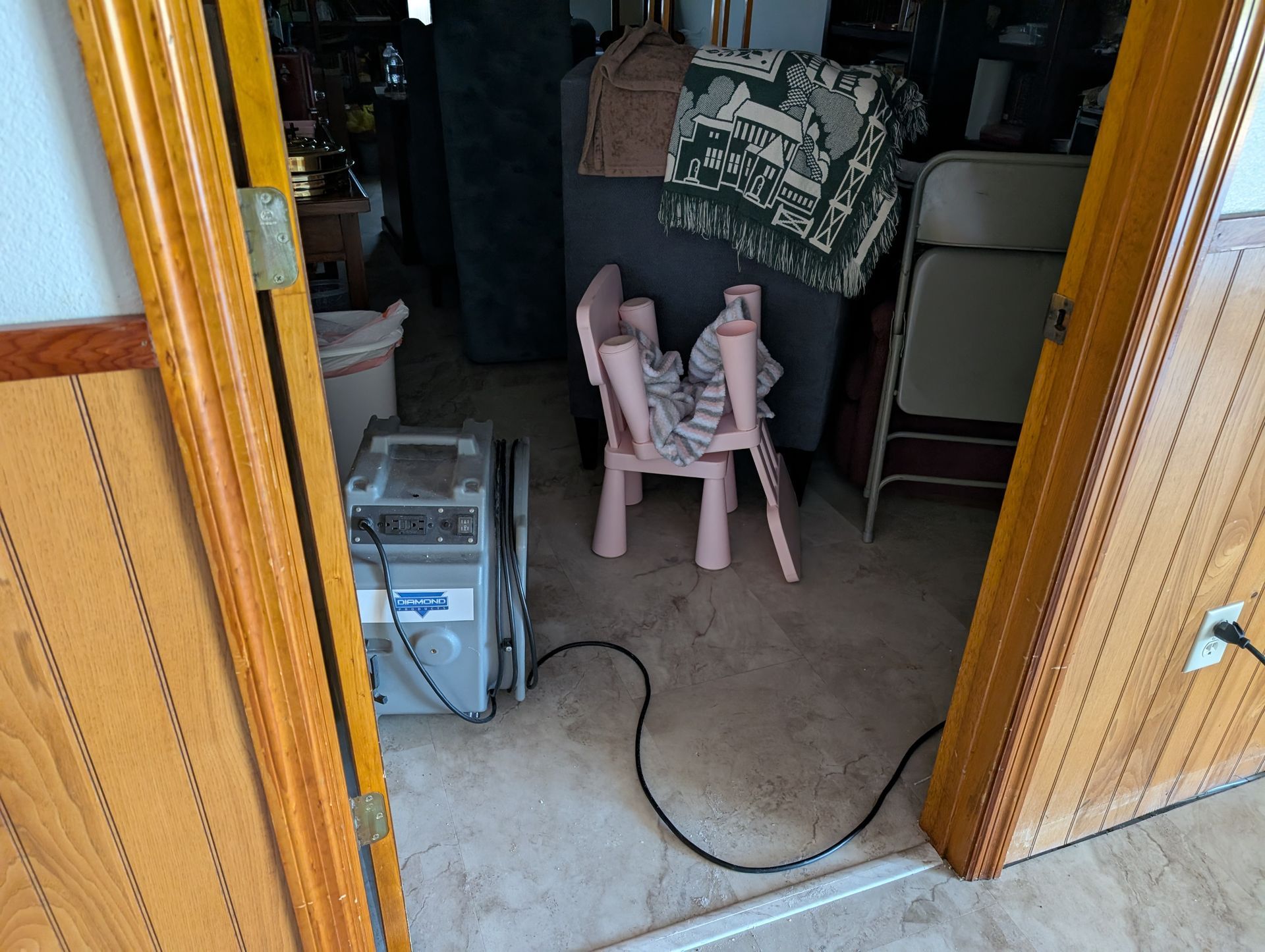 Open doorway with a dehumidifier, a child's chair, and various items in a cluttered room.