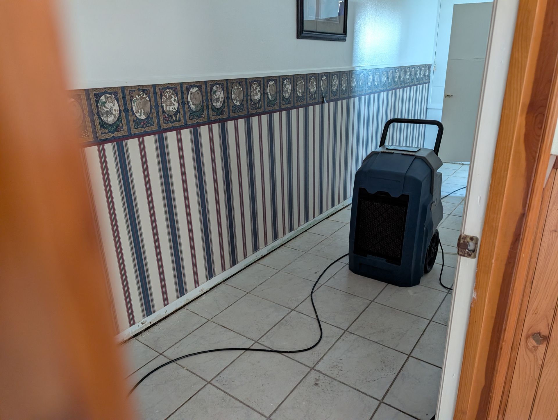 Dehumidifier in a room with striped wallpaper and tiled floor, possibly for water damage.