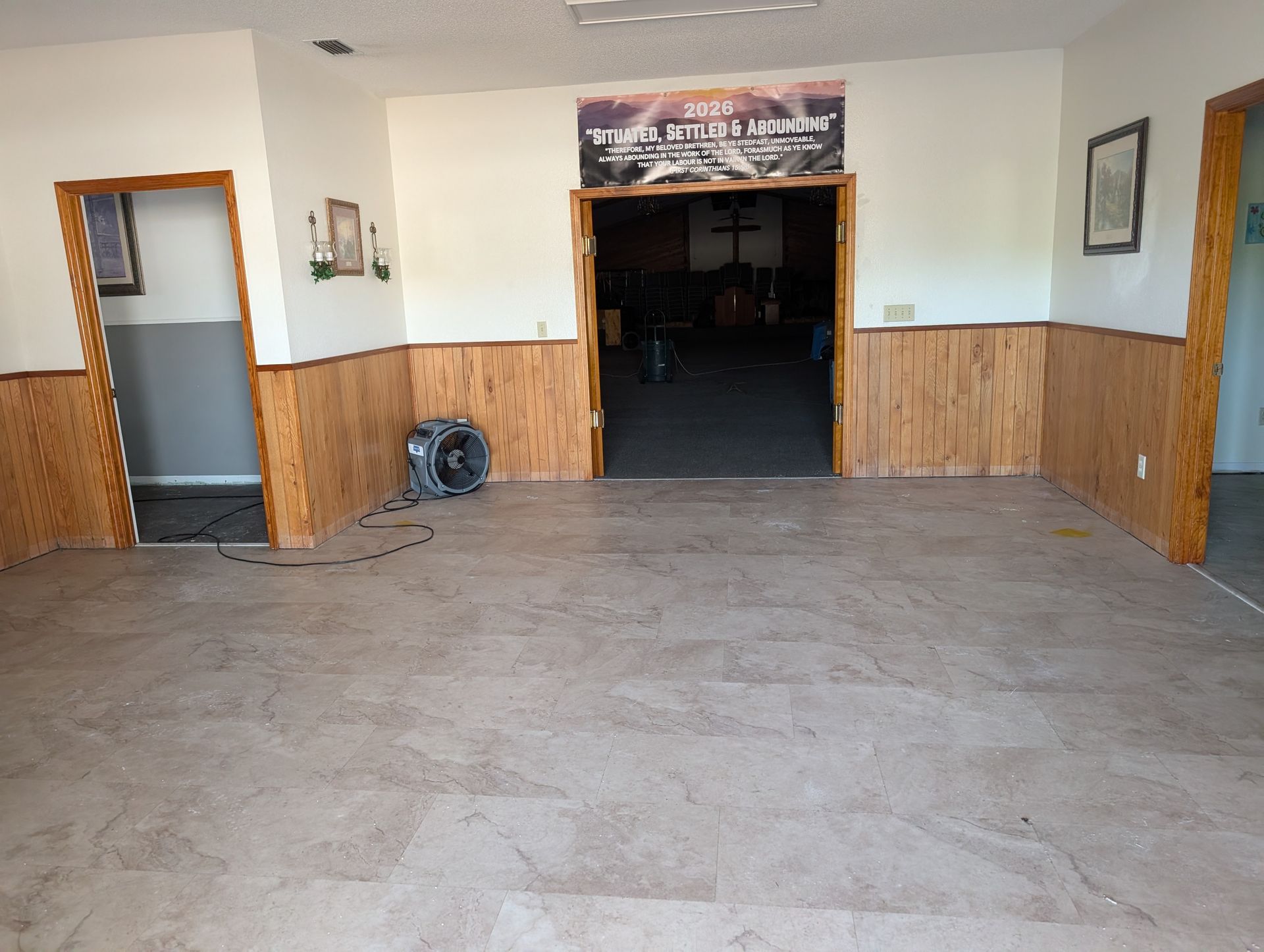 Empty room with wood paneling, open doorways, and a fan. Dark flooring, cream and gray walls.