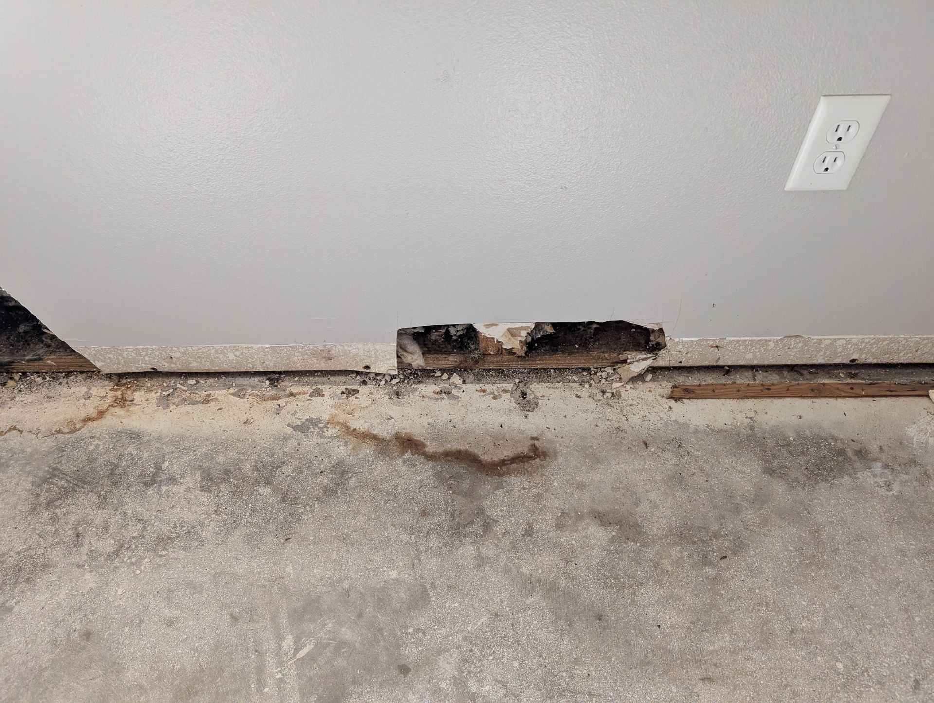 Damaged wall section with a hole, potentially water damaged. Electrical outlet visible above.