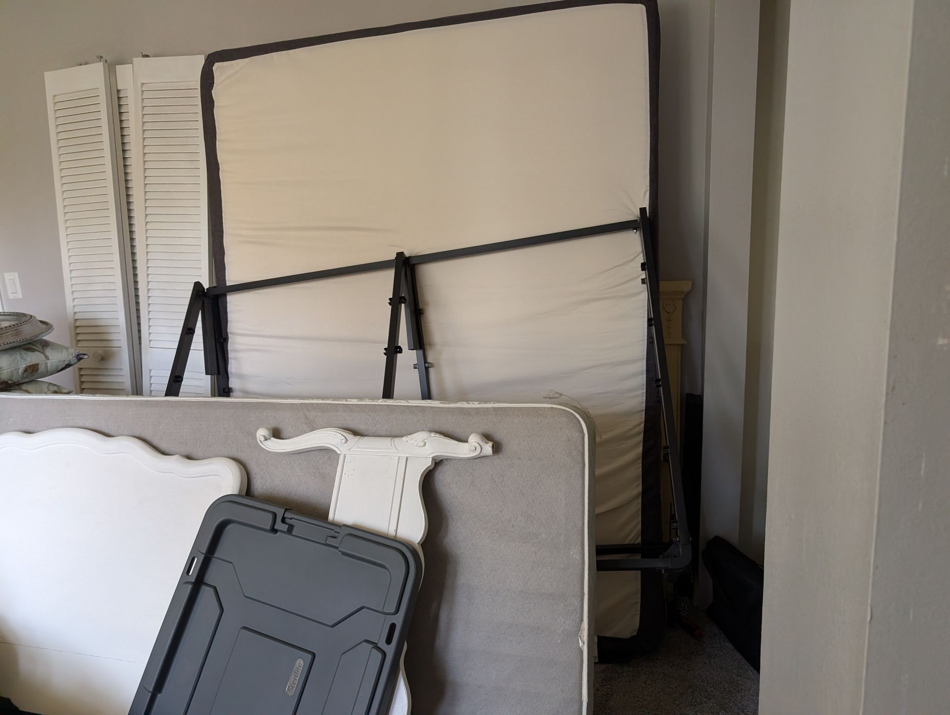 A mattress, box spring, and other items are stacked against a wall inside a room.