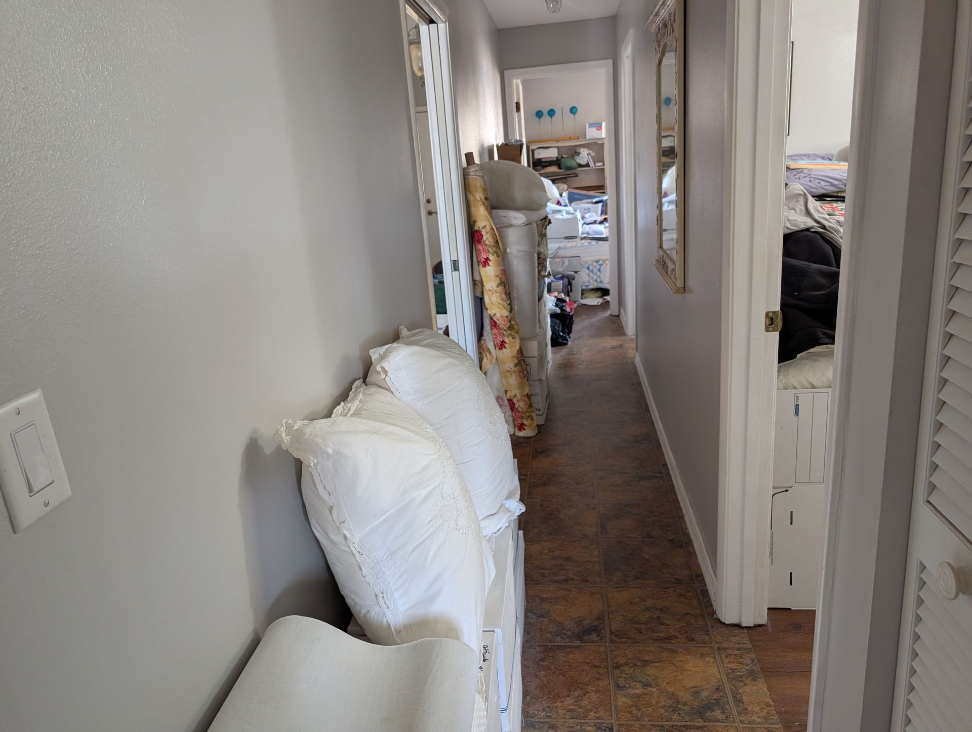 Narrow hallway with stacked pillows and rolled rugs on the left, open door on the right.