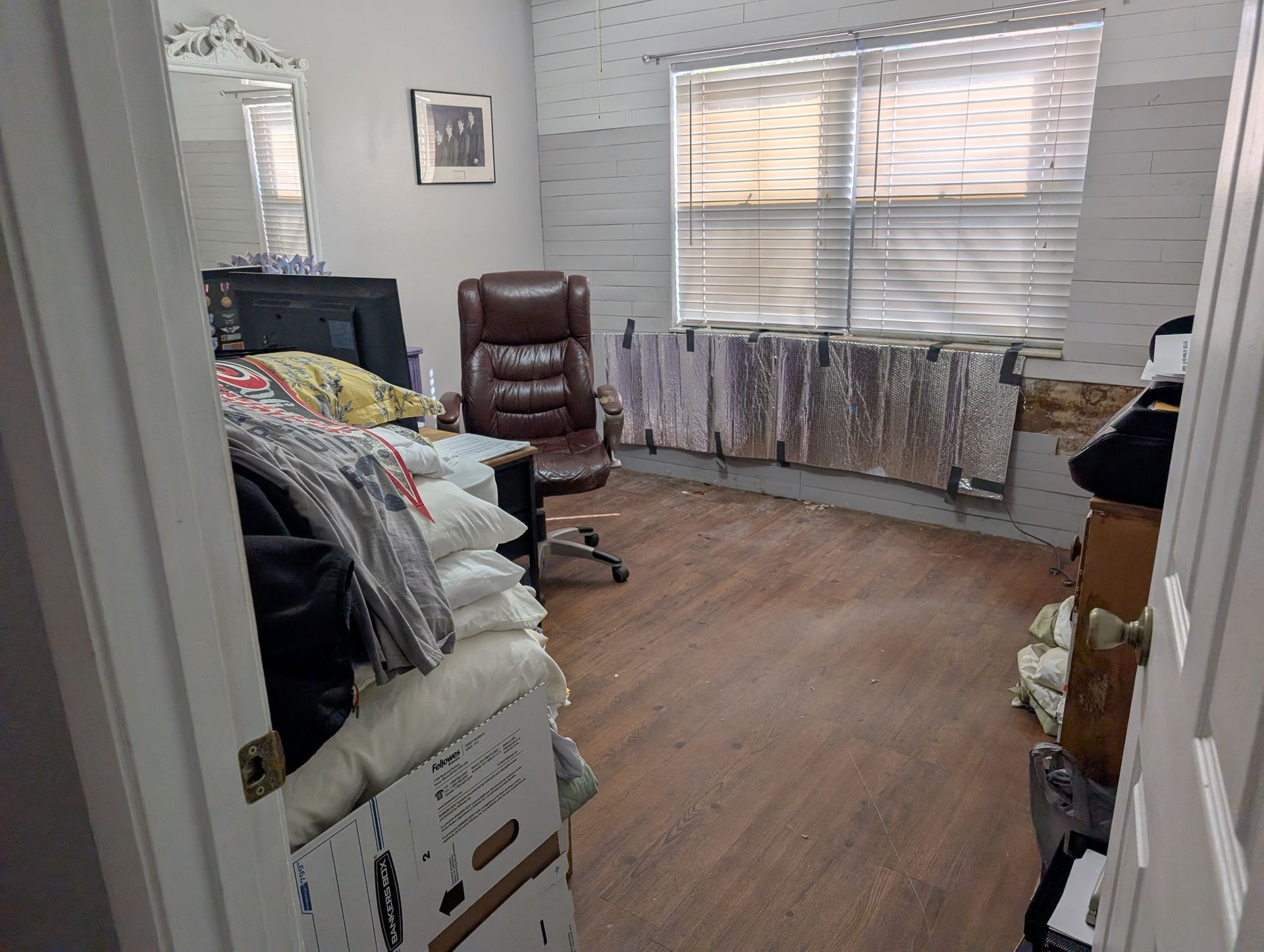 Cluttered office with brown desk chair, window, piles of items, and partially painted walls.