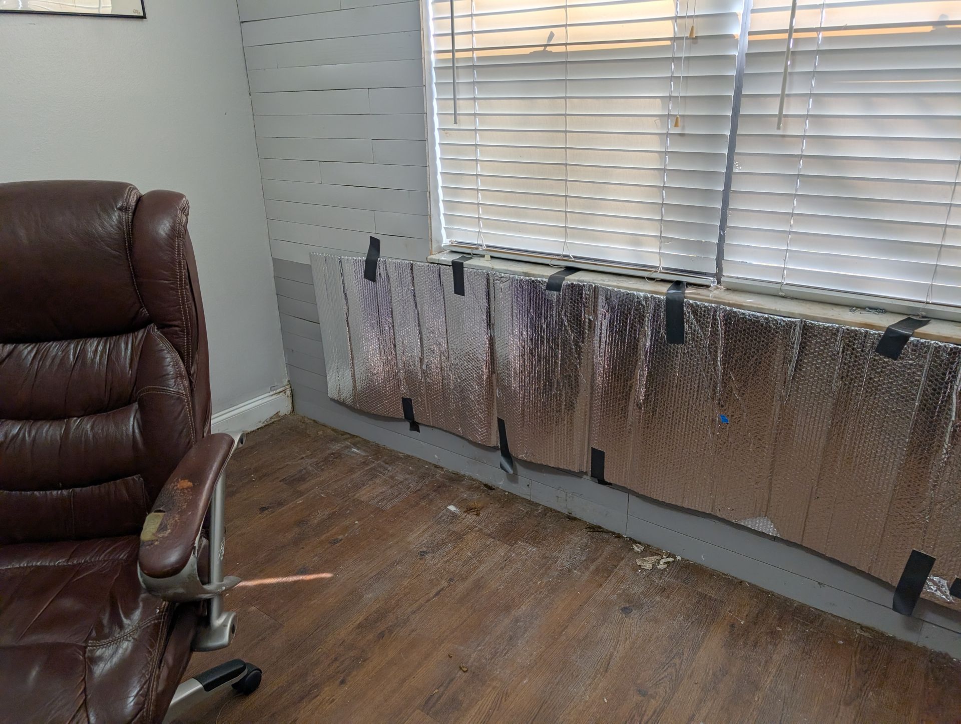 A room with a chair, window covered in foil insulation, and peeling floor.