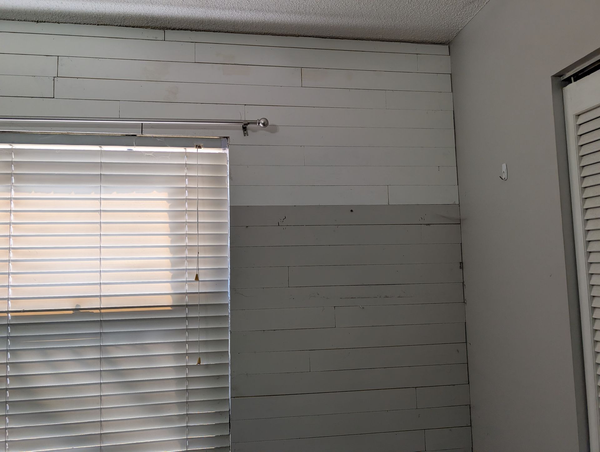 Interior wall with horizontal white and grey planks, window with blinds, and door.