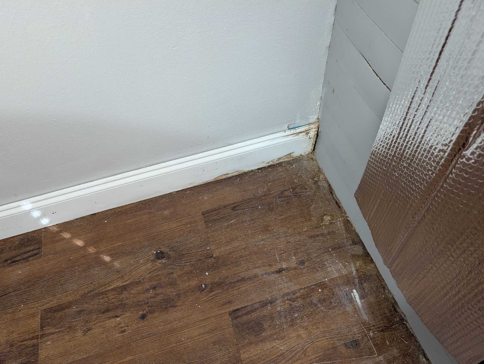 Corner of a room with white walls, brown wood-look flooring, and insulation.