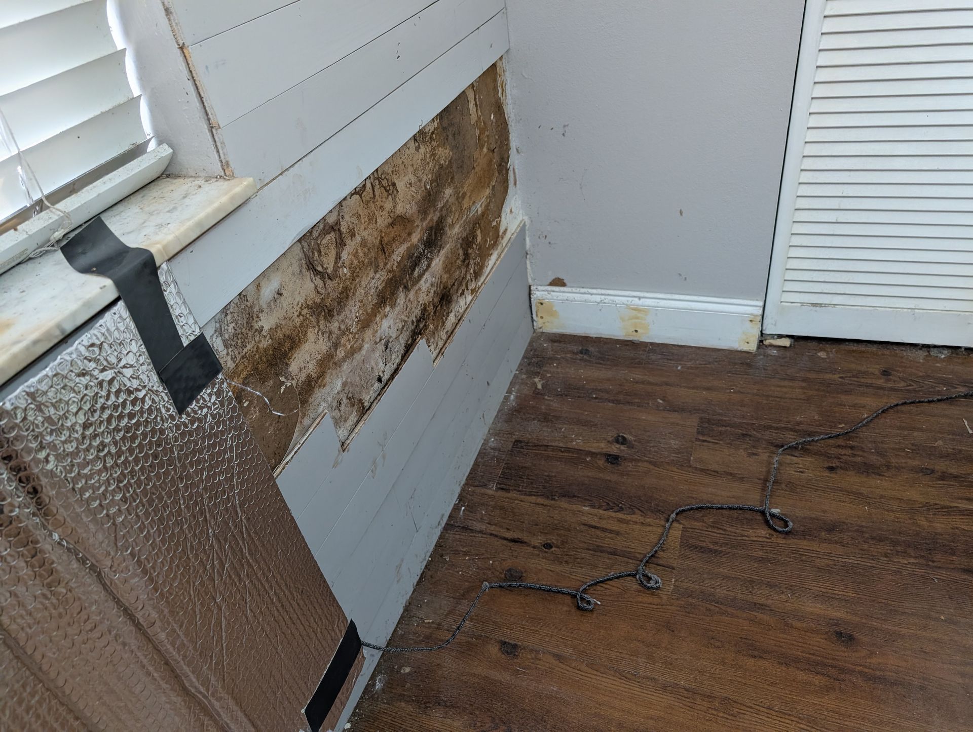 Wall with exposed damage, wood siding partially removed, interior damage visible, and window blinds.