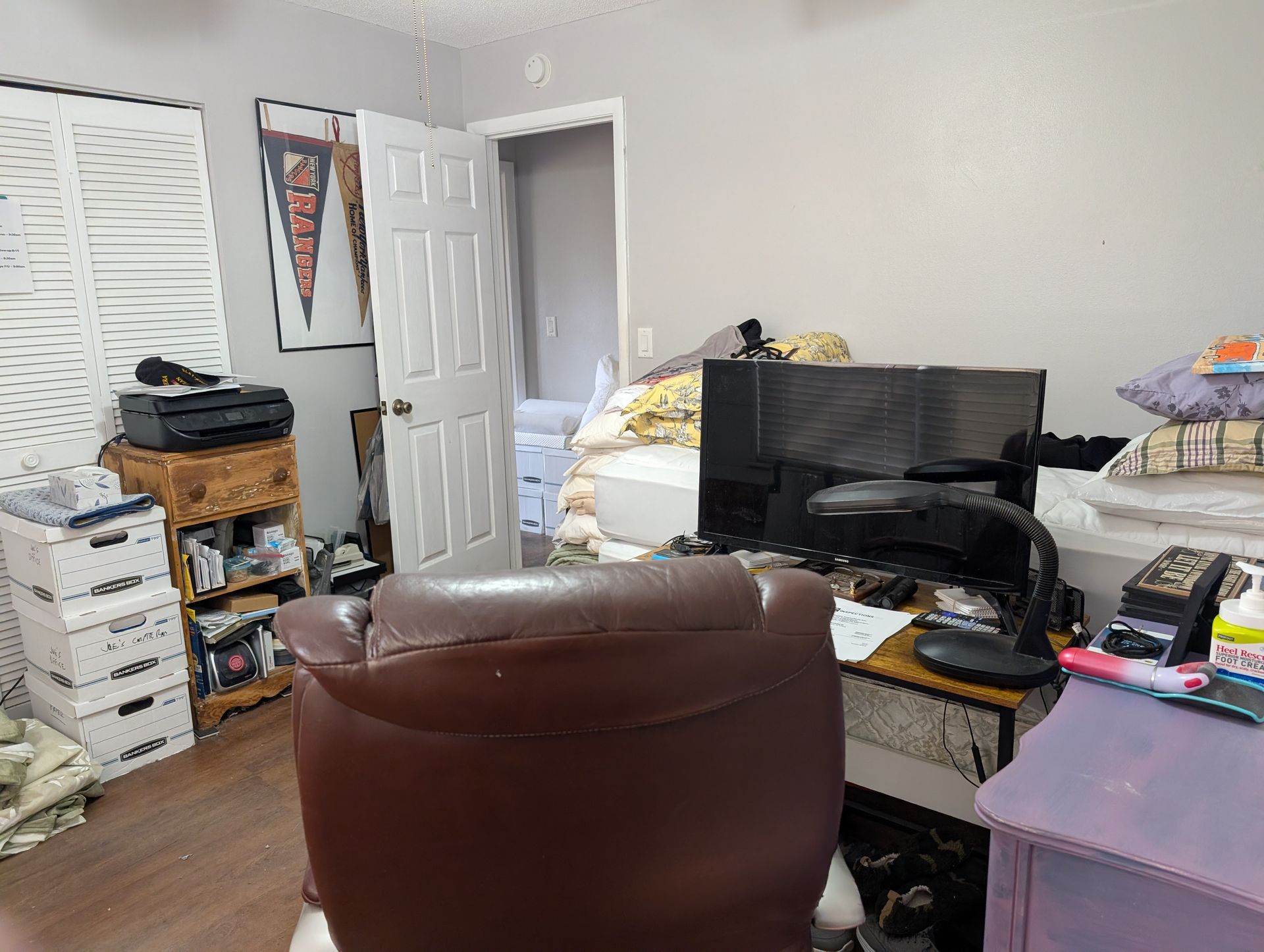 Cluttered bedroom with desk, recliner, storage, door to another room, and several other items.