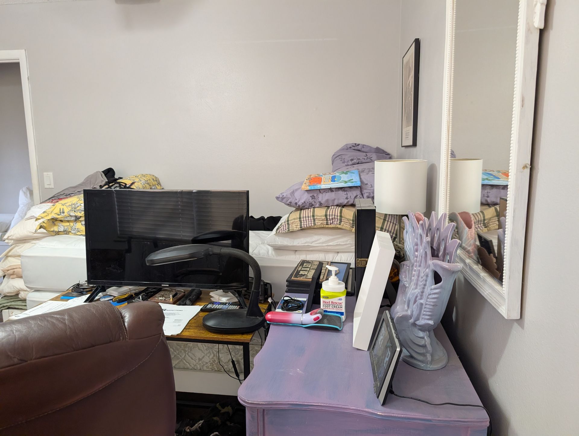 A cluttered room with a bed, desk, mirror, and various items.