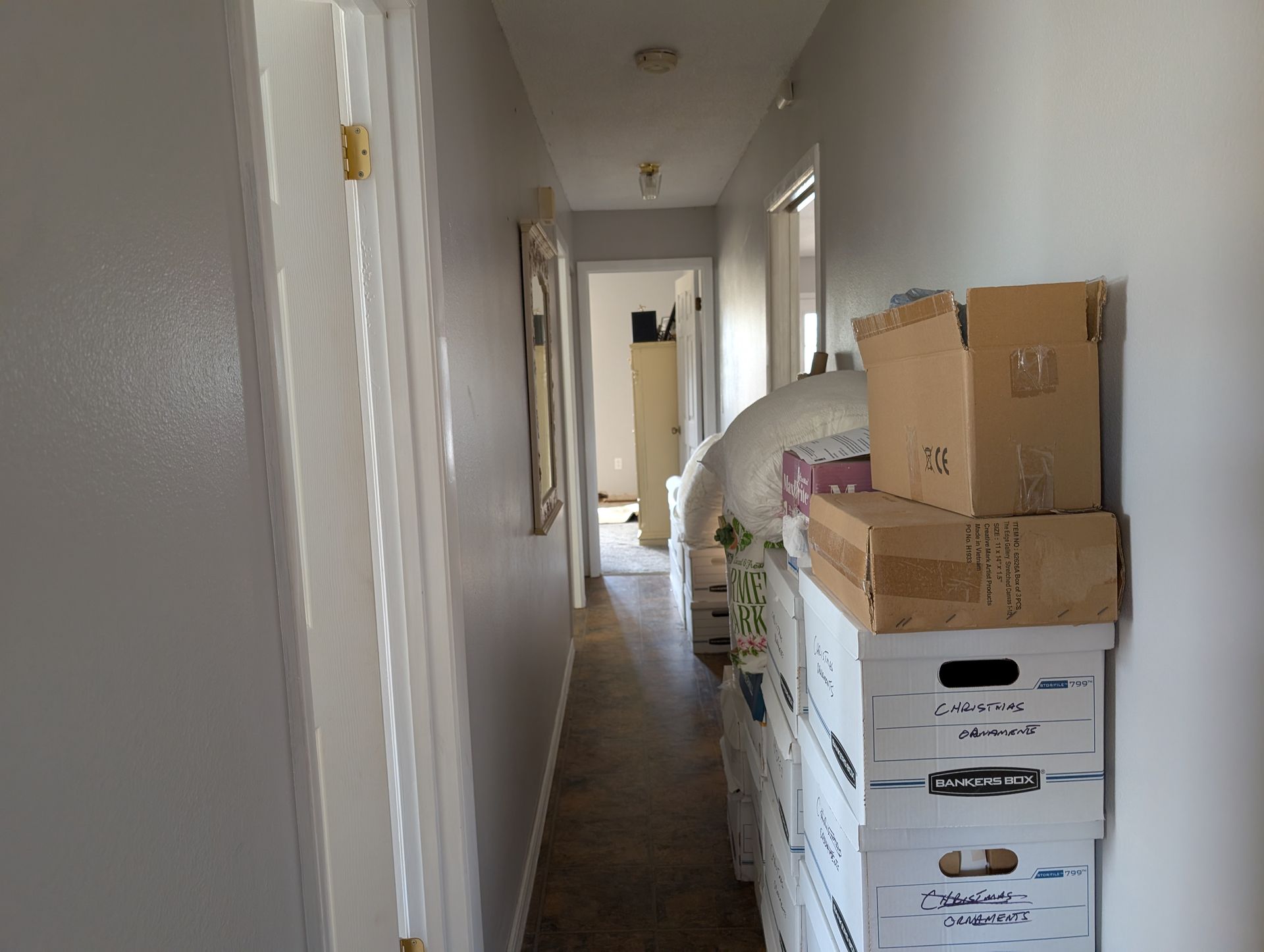 Narrow hallway with boxes stacked against the wall, leading to a door at the end.