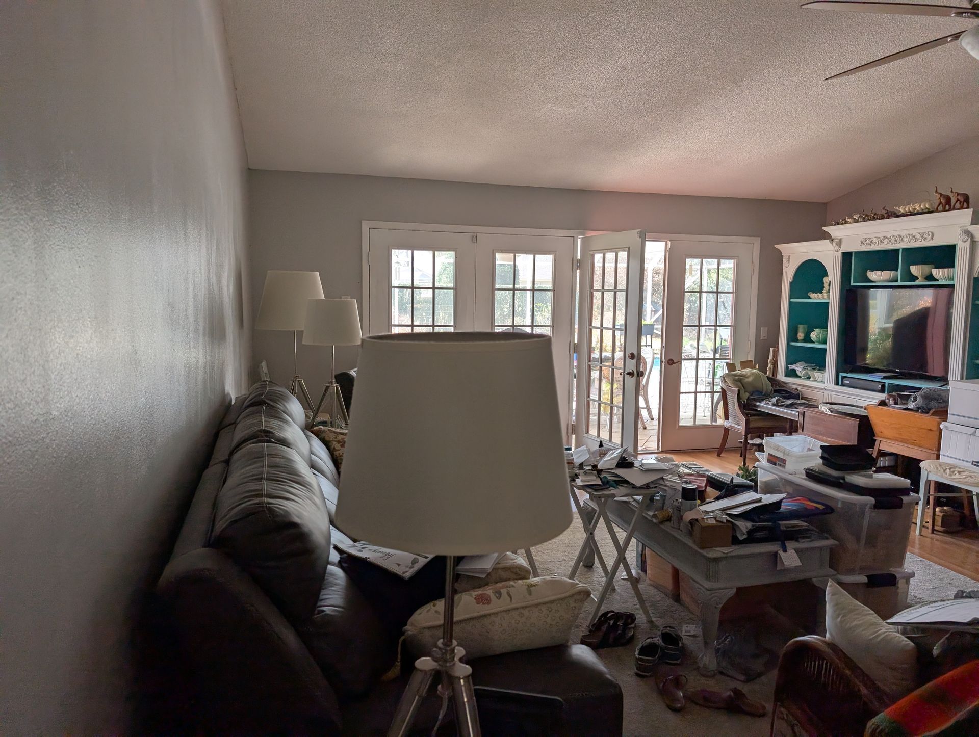 Living room with couch, lamp, French doors, cluttered table, and built-in cabinet with a TV.