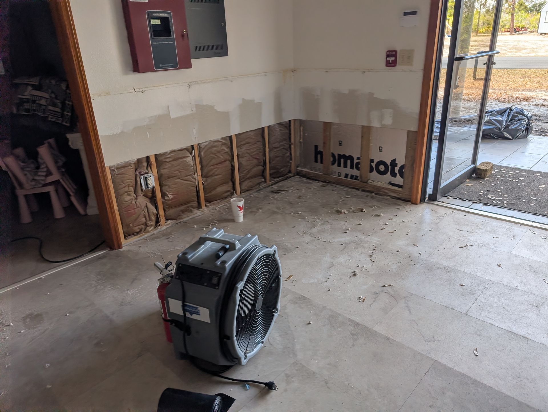 Garage interior with water damage, exposed framing, a fan, debris, and an open door.