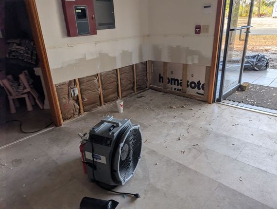 Garage interior with exposed walls and fan, likely drying after water damage.