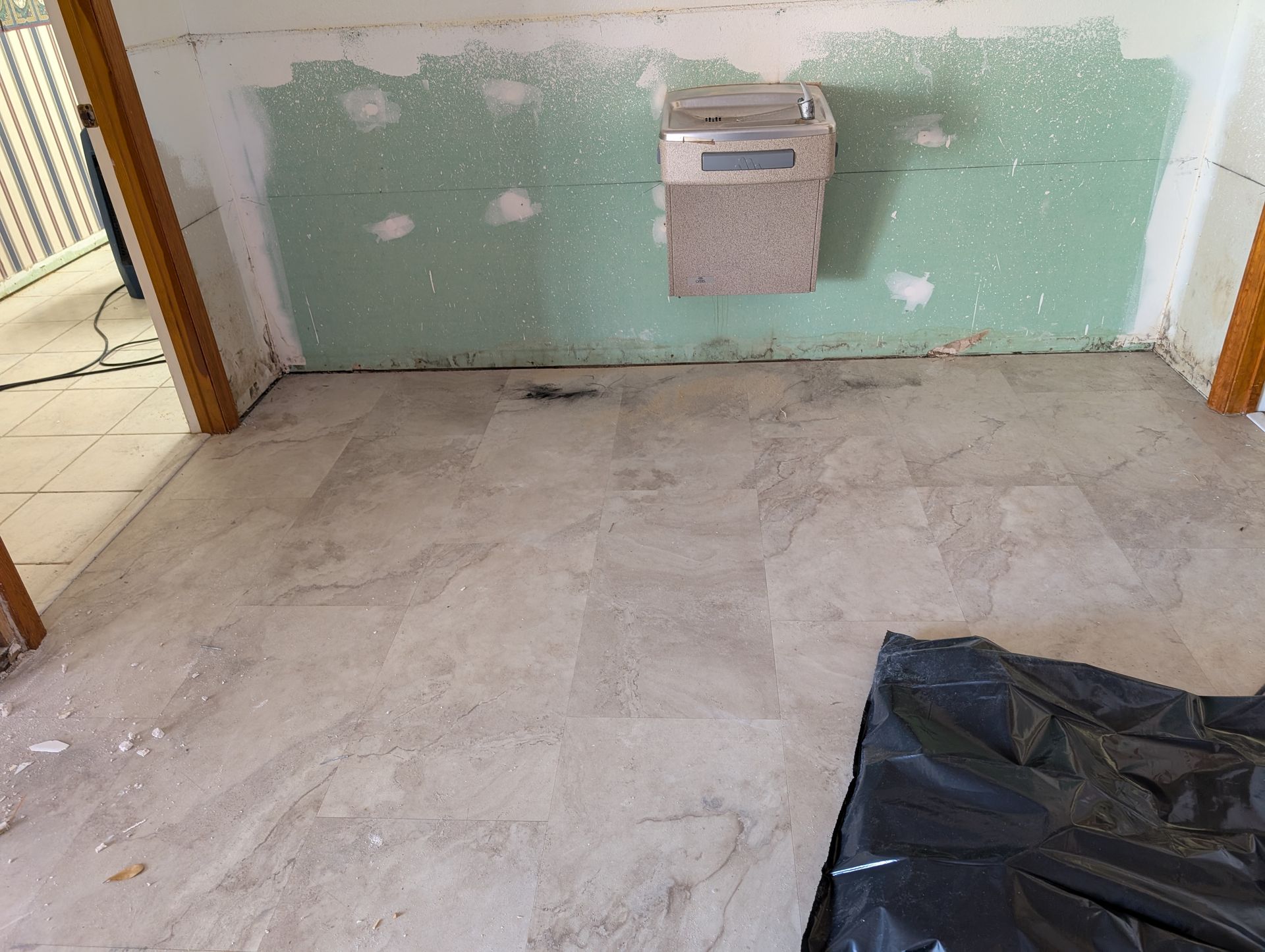 Room under renovation with damaged walls, floor, and a water fountain.
