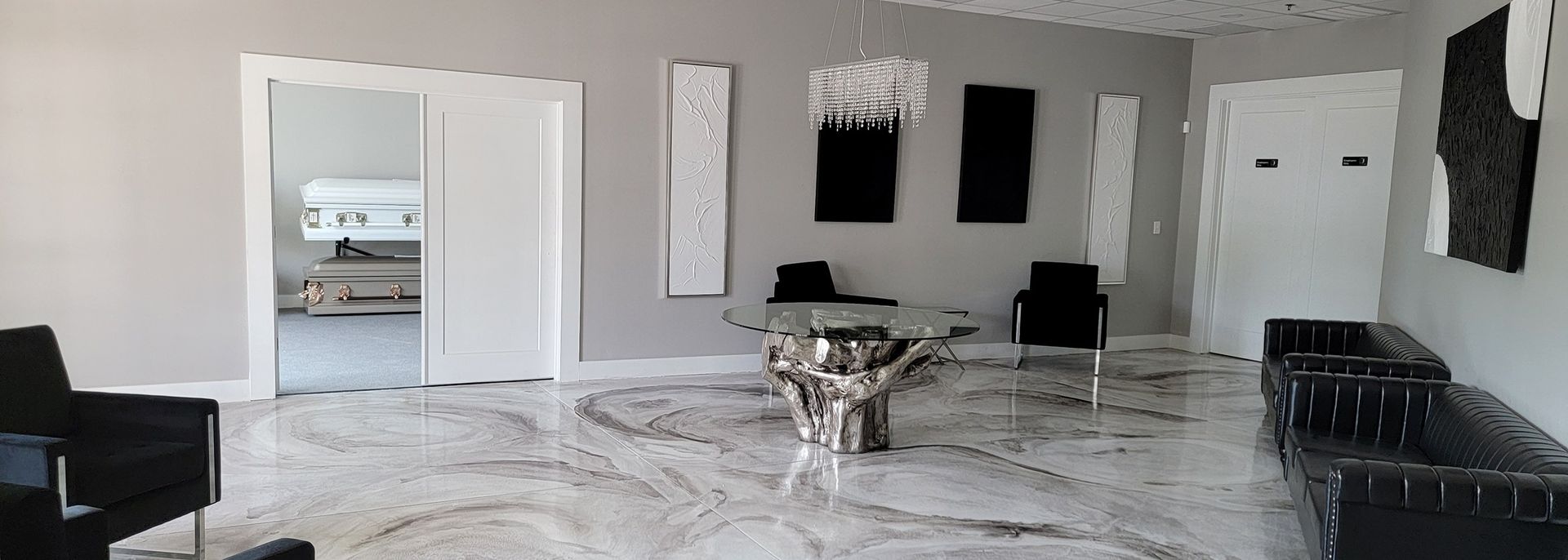 Modern living room with marble floor, white walls, black wall art, and a glass coffee table