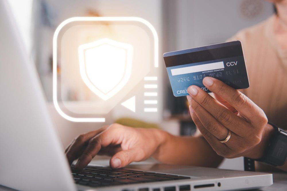 Personne utilisant un ordinateur portable et une carte de crédit, avec une icône de bouclier de sécurité superposée.