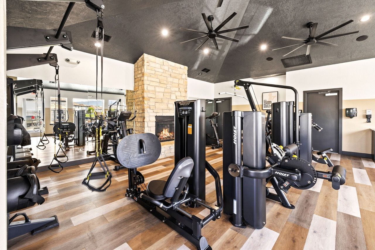 Indoor community gym with cardio and strength machines, mirrors, and a stone fireplace.